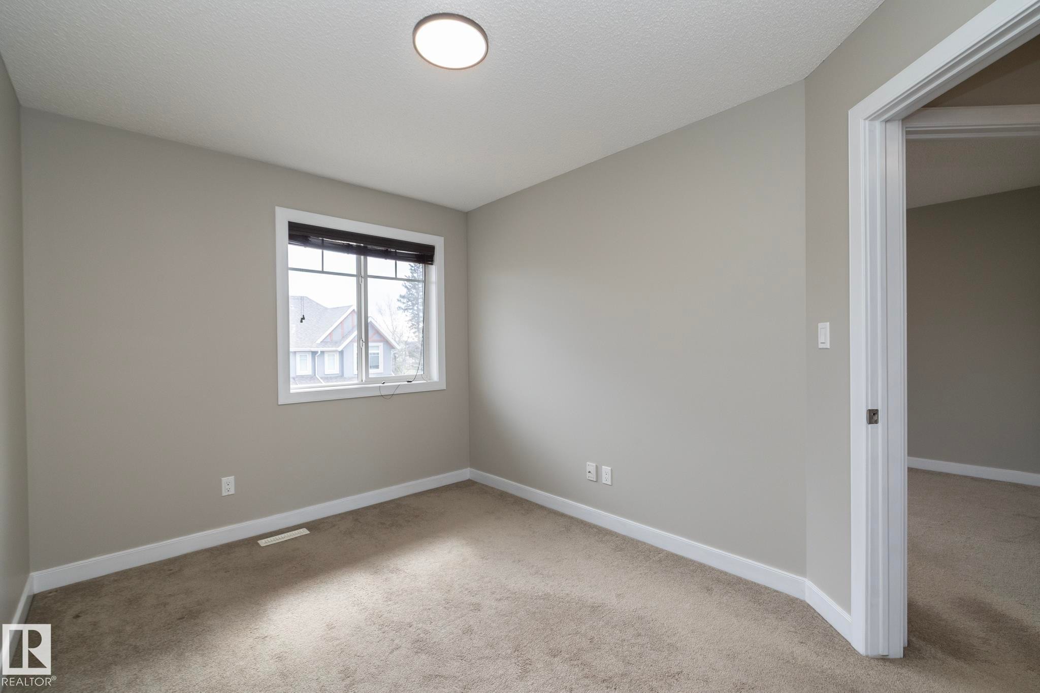 Neutral toned walls and carpeting, featuring a window with dark blinds and a single ceiling light fixture - 117 Callaghan Drive Sw, Edmonton, AB - Indoor Photo Showing Other Room