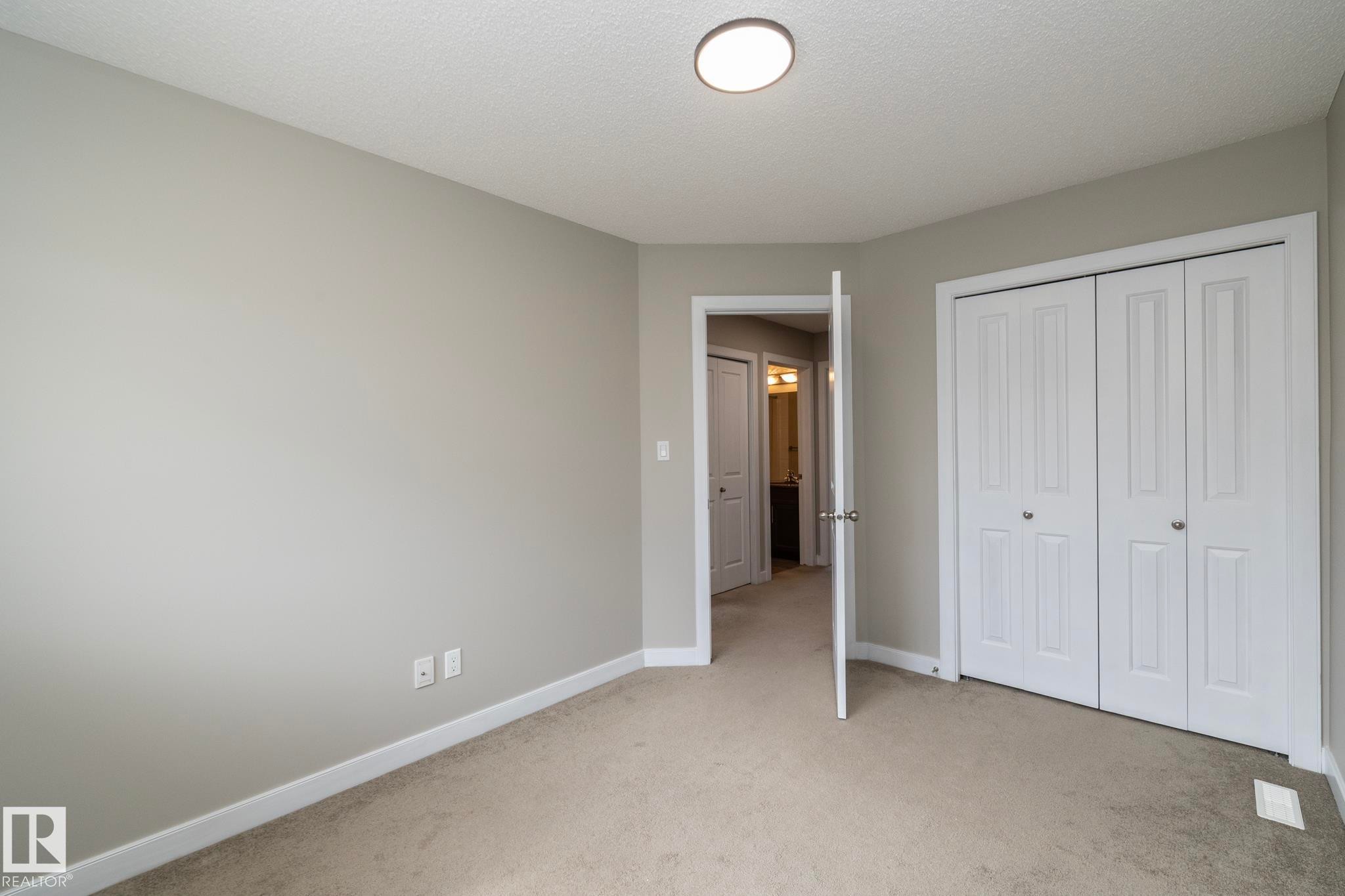 Room featuring neutral wall tones, carpeted flooring, a flush-mount ceiling light, white bi-fold closet doors, and white trim - 117 Callaghan Drive Sw, Edmonton, AB - Indoor