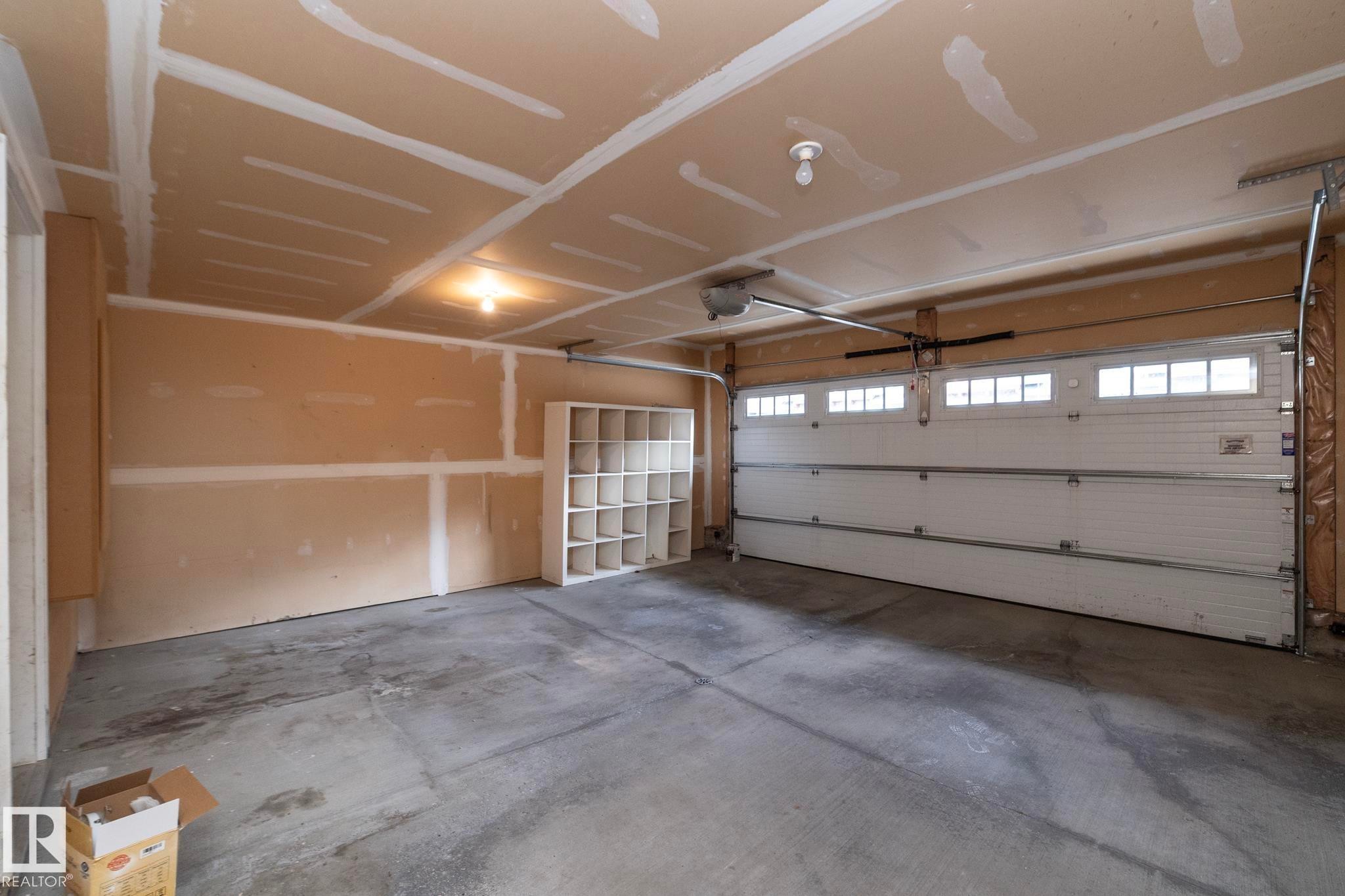 Spacious garage featuring a concrete floor, exposed drywall walls, and a white overhead door with transom windows - 117 Callaghan Drive Sw, Edmonton, AB - Indoor Photo Showing Garage