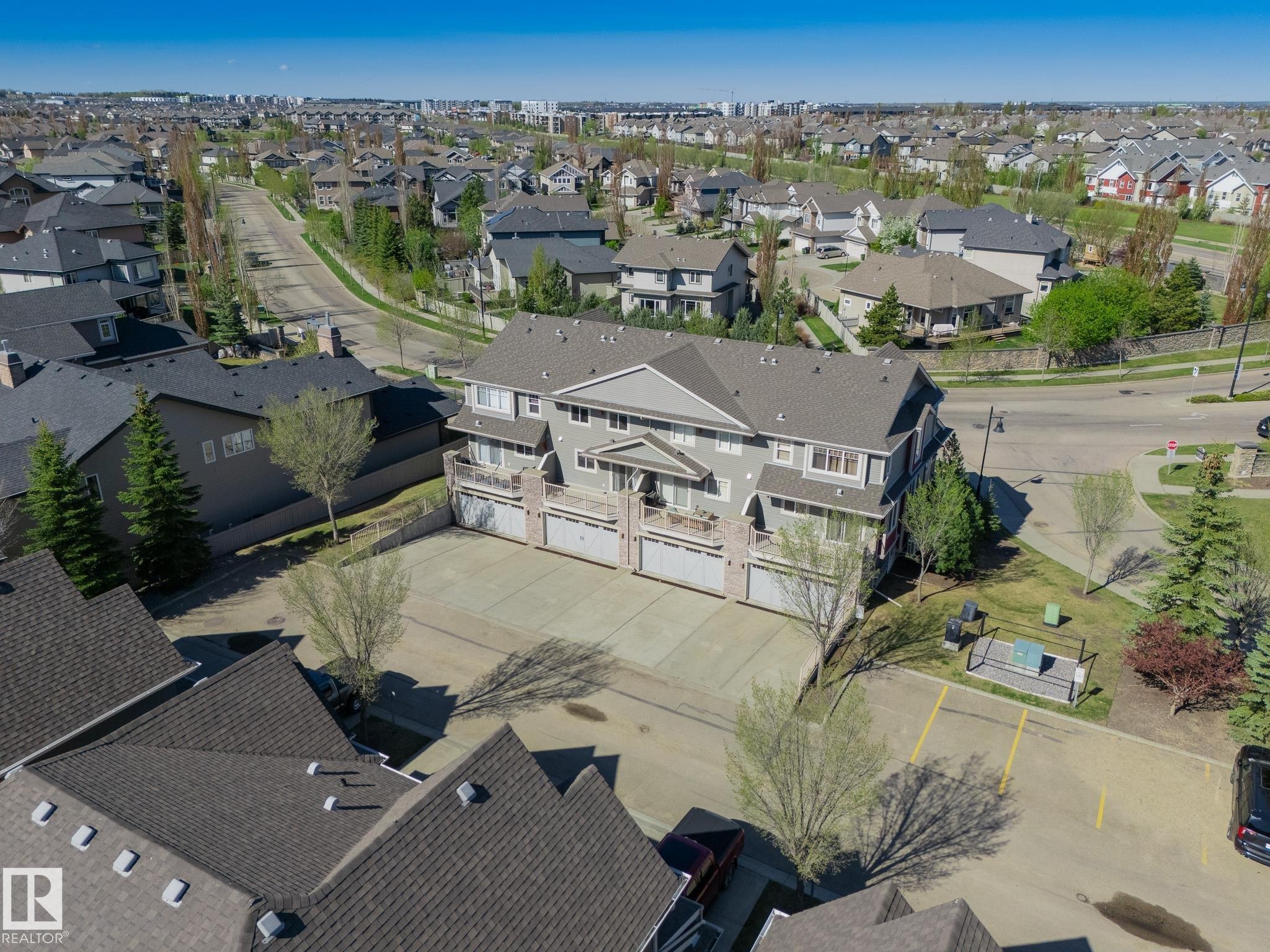 Multi-level residential building featuring private balconies, individual garage doors, and a paved parking area - 117 Callaghan Drive Sw, Edmonton, AB - Outdoor With View