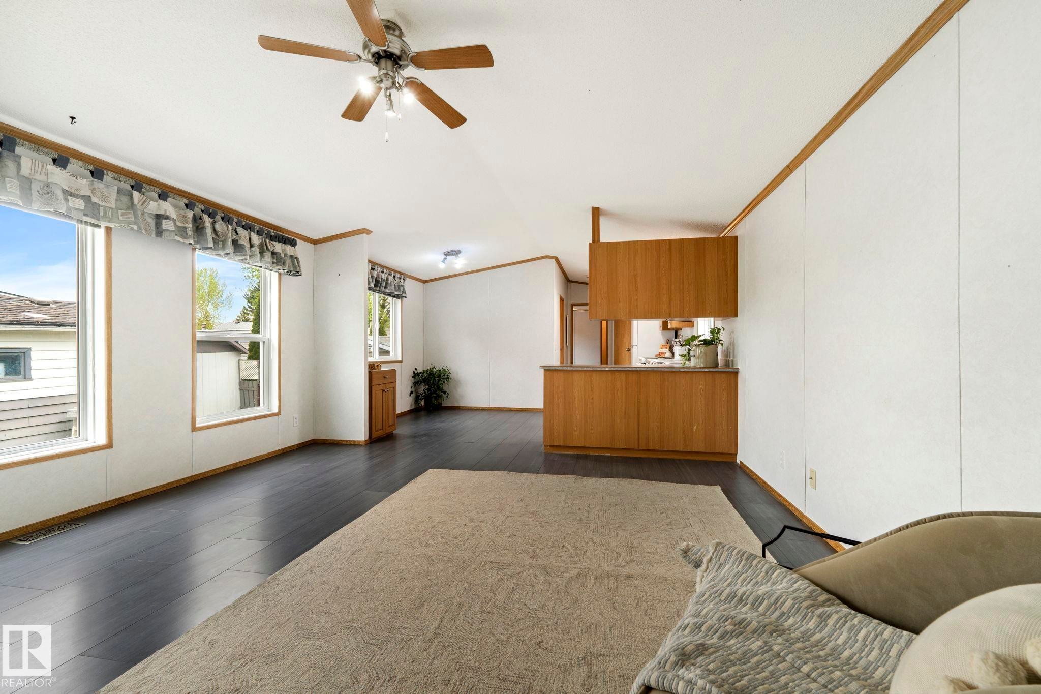 Spacious living area featuring dark wood-finish flooring, white paneled walls, and multiple large windows - 49 Rim Road Nw, Edmonton, AB - Indoor