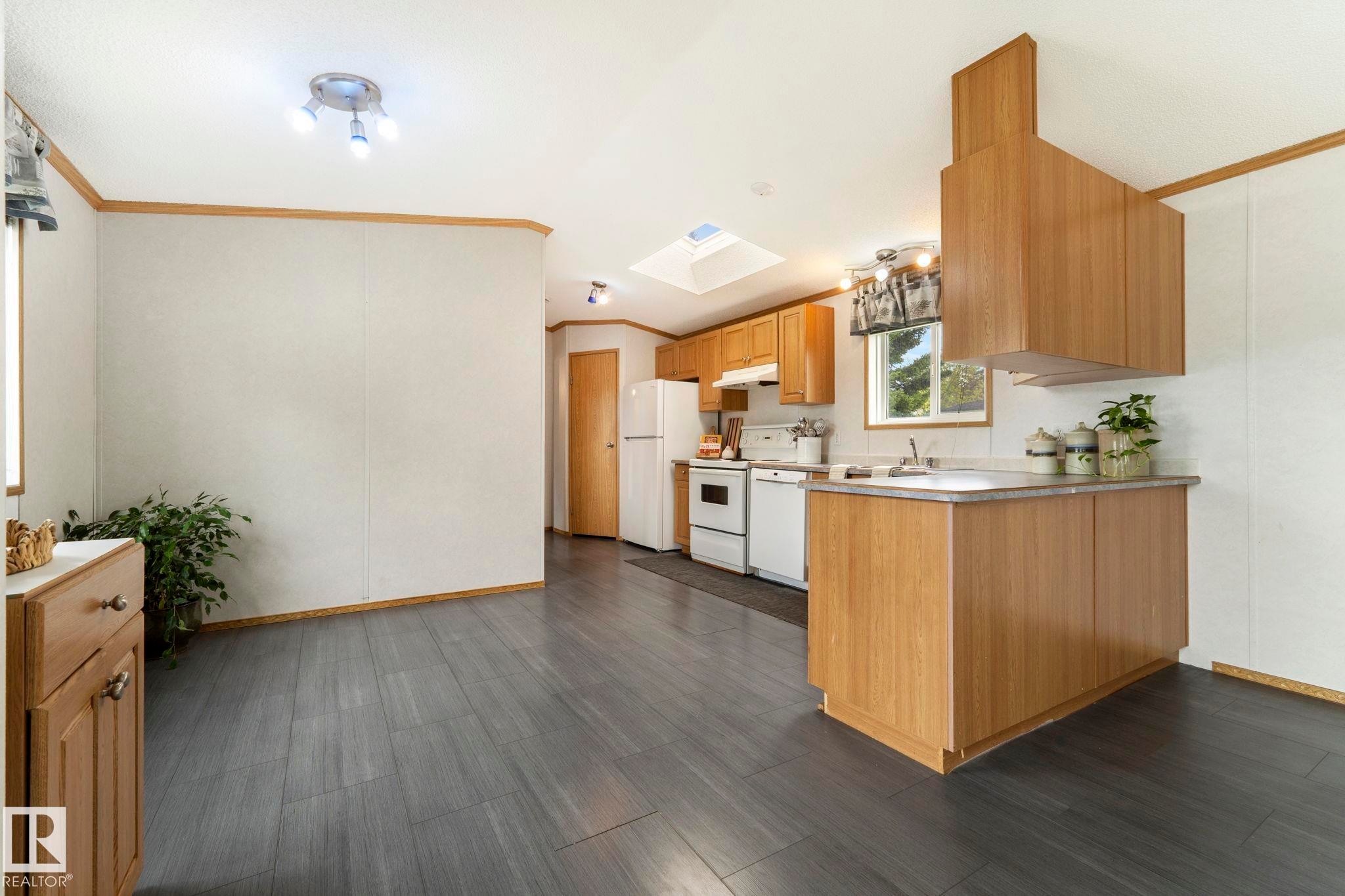 Open-concept kitchen and dining area featuring wood-finish flooring, wood cabinetry, a skylight, and white appliances - 49 Rim Road Nw, Edmonton, AB - Indoor Photo Showing Kitchen