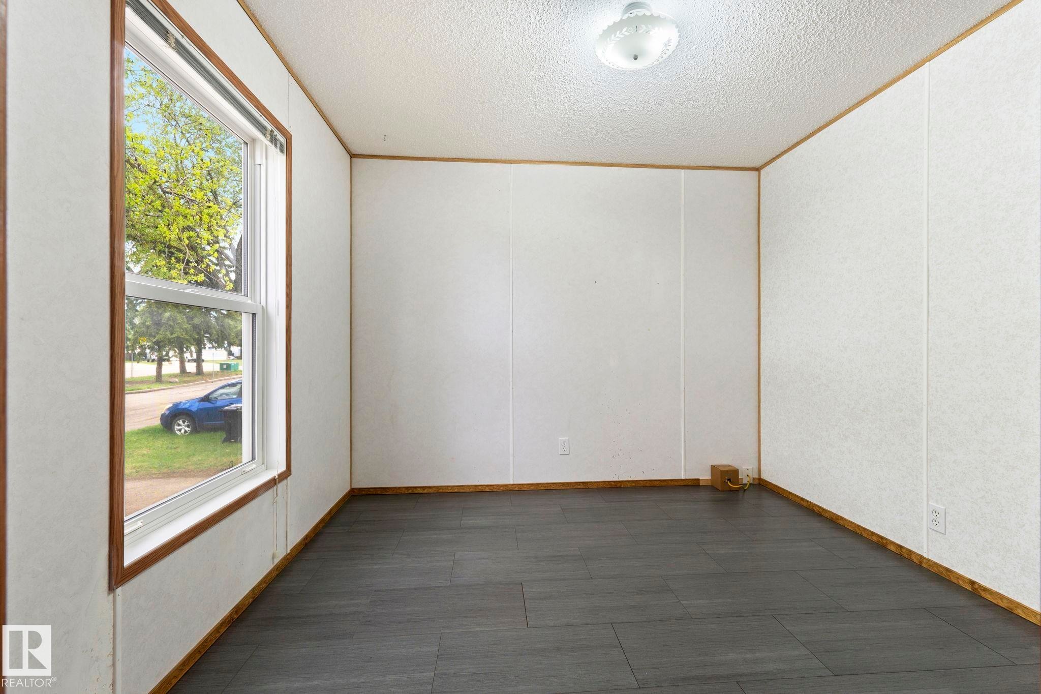 Spacious room featuring dark wood-finish flooring, white panel walls, and a large window with wood trim - 49 Rim Road Nw, Edmonton, AB - Indoor Photo Showing Other Room