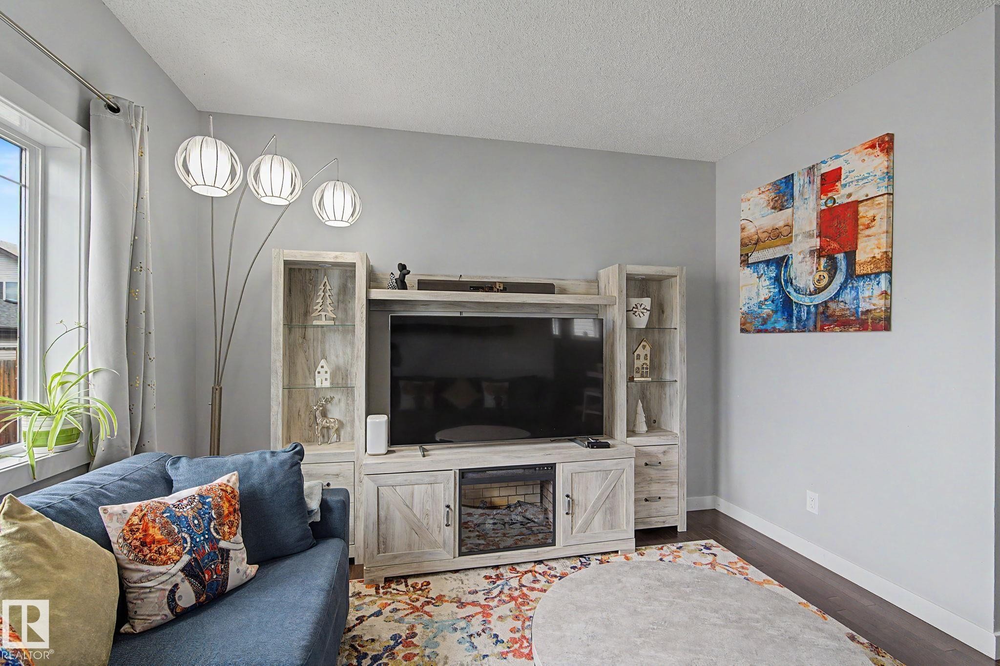 Integrated entertainment center with an electric fireplace, display cabinetry, and dark wood-finish flooring - 18144 76 Street Nw, Edmonton, AB - Indoor Photo Showing Living Room