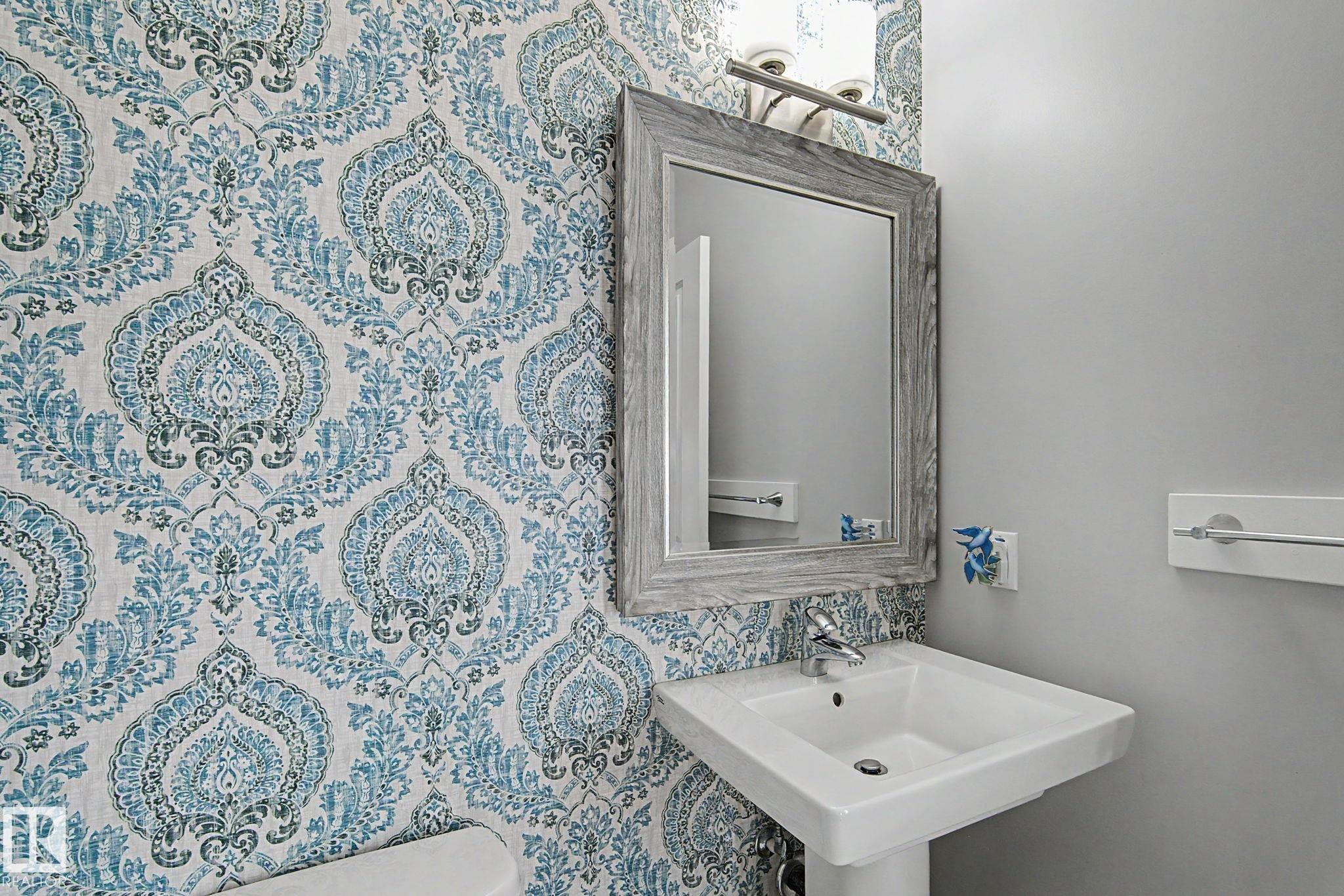 Pedestal sink with chrome faucet, framed mirror, and decorative wall sconce - 18144 76 Street Nw, Edmonton, AB - Indoor Photo Showing Bathroom