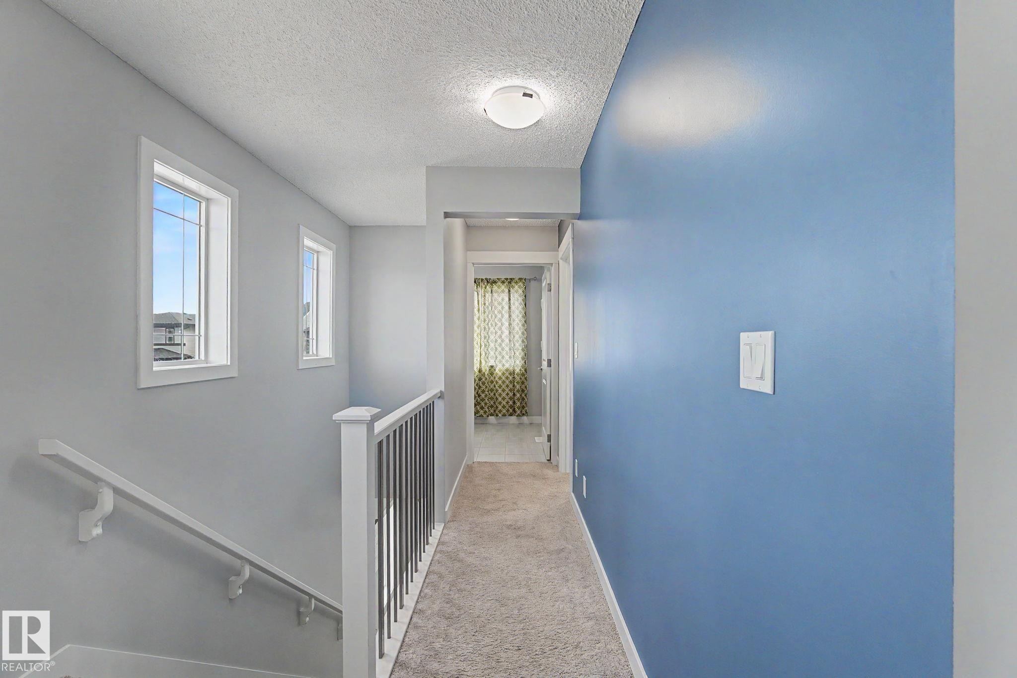 Upper-level landing featuring light gray walls, a contrasting blue accent wall, and textured carpeting - 18144 76 Street Nw, Edmonton, AB - Indoor Photo Showing Other Room