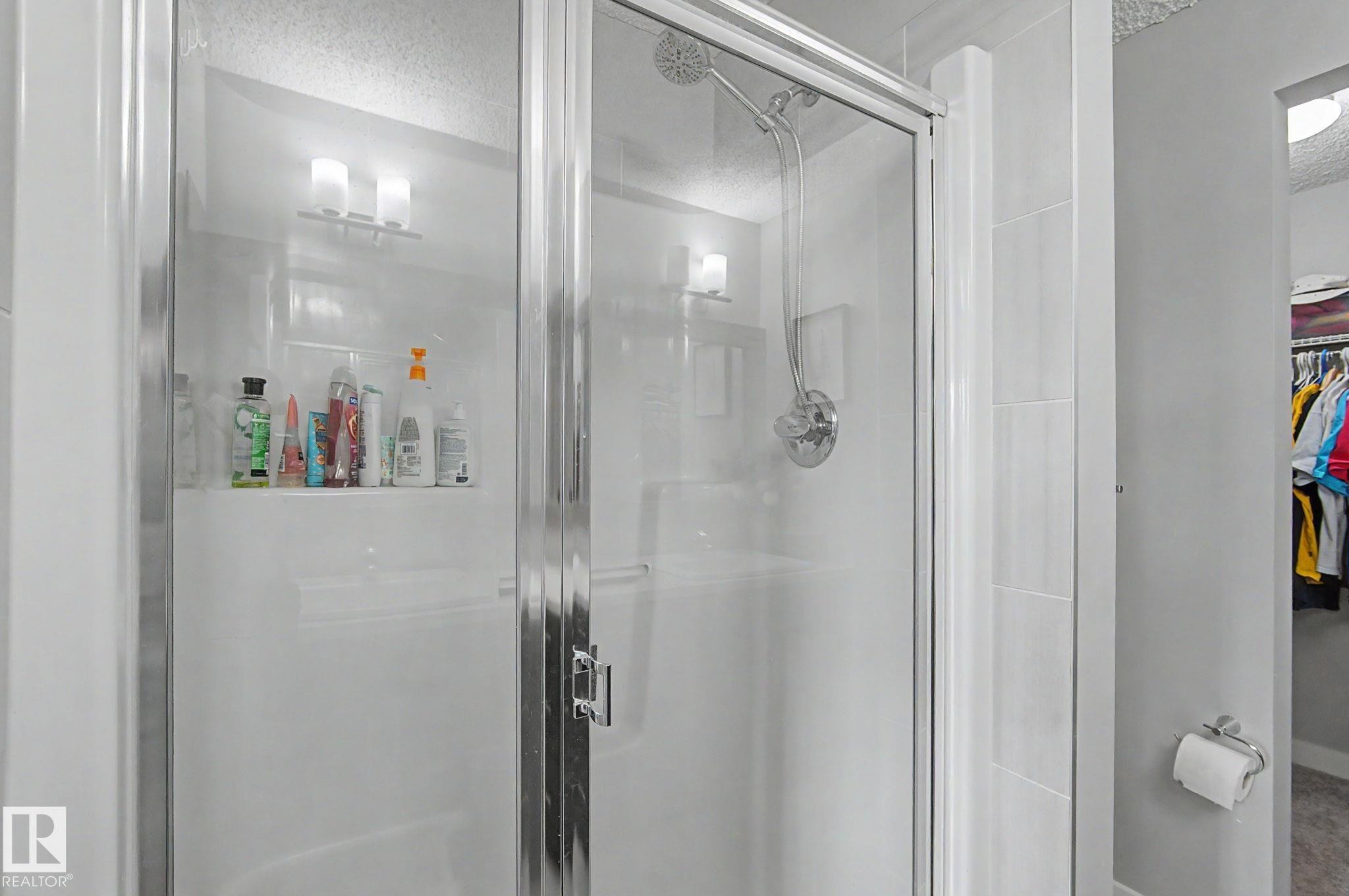 Glass-enclosed shower with a sliding door, featuring a built-in shower niche, chrome fixtures, and white tile surround - 18144 76 Street Nw, Edmonton, AB - Indoor Photo Showing Bathroom