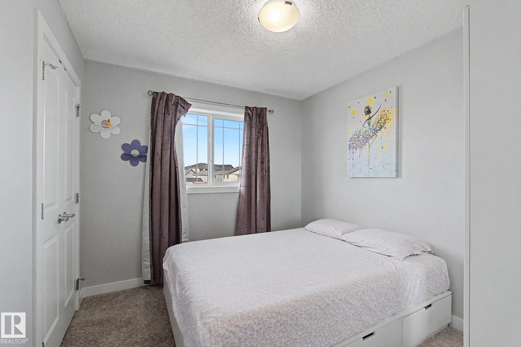 Bedroom featuring neutral wall paint, carpet flooring, a window with curtains, a ceiling-mounted light fixture, and a white paneled door - 18144 76 Street Nw, Edmonton, AB - Indoor Photo Showing Bedroom