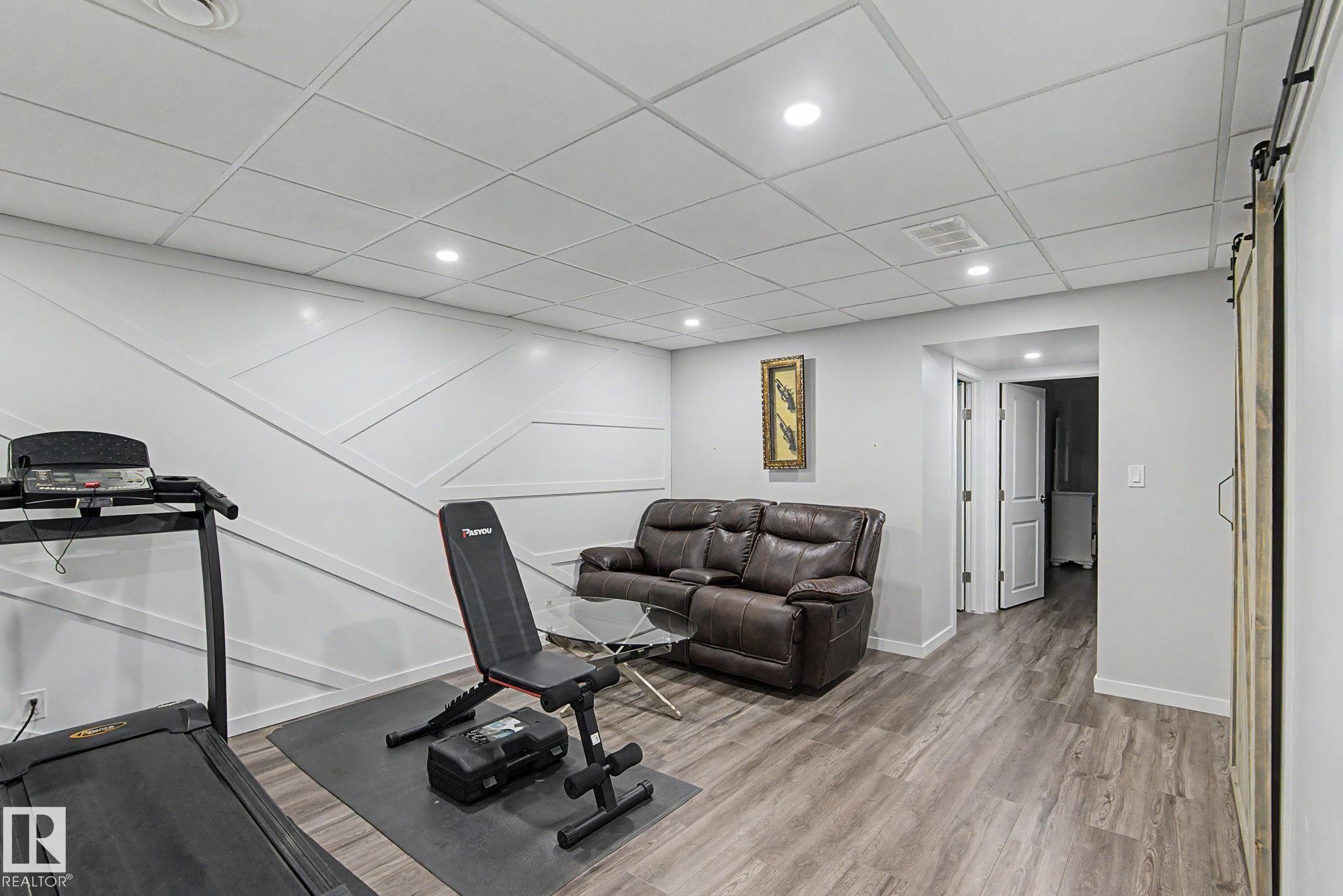 Recreation room featuring wood-finish flooring, a contemporary accent wall, recessed lighting, and a barn door - 18144 76 Street Nw, Edmonton, AB - Indoor