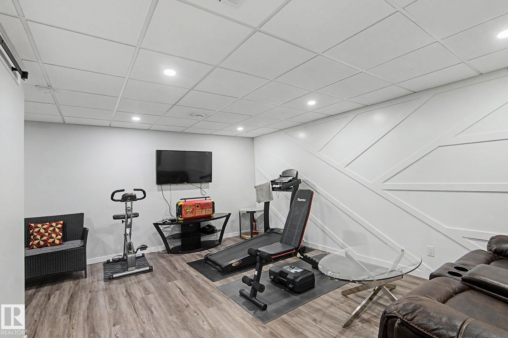 Spacious recreation room featuring wood-finish flooring, recessed lighting, and a decorative accent wall with geometric paneling - 18144 76 Street Nw, Edmonton, AB - Indoor Photo Showing Gym Room
