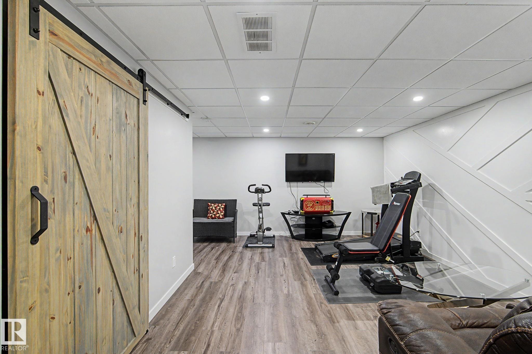 Distressed wood-finish barn door with matte black hardware - 18144 76 Street Nw, Edmonton, AB - Indoor