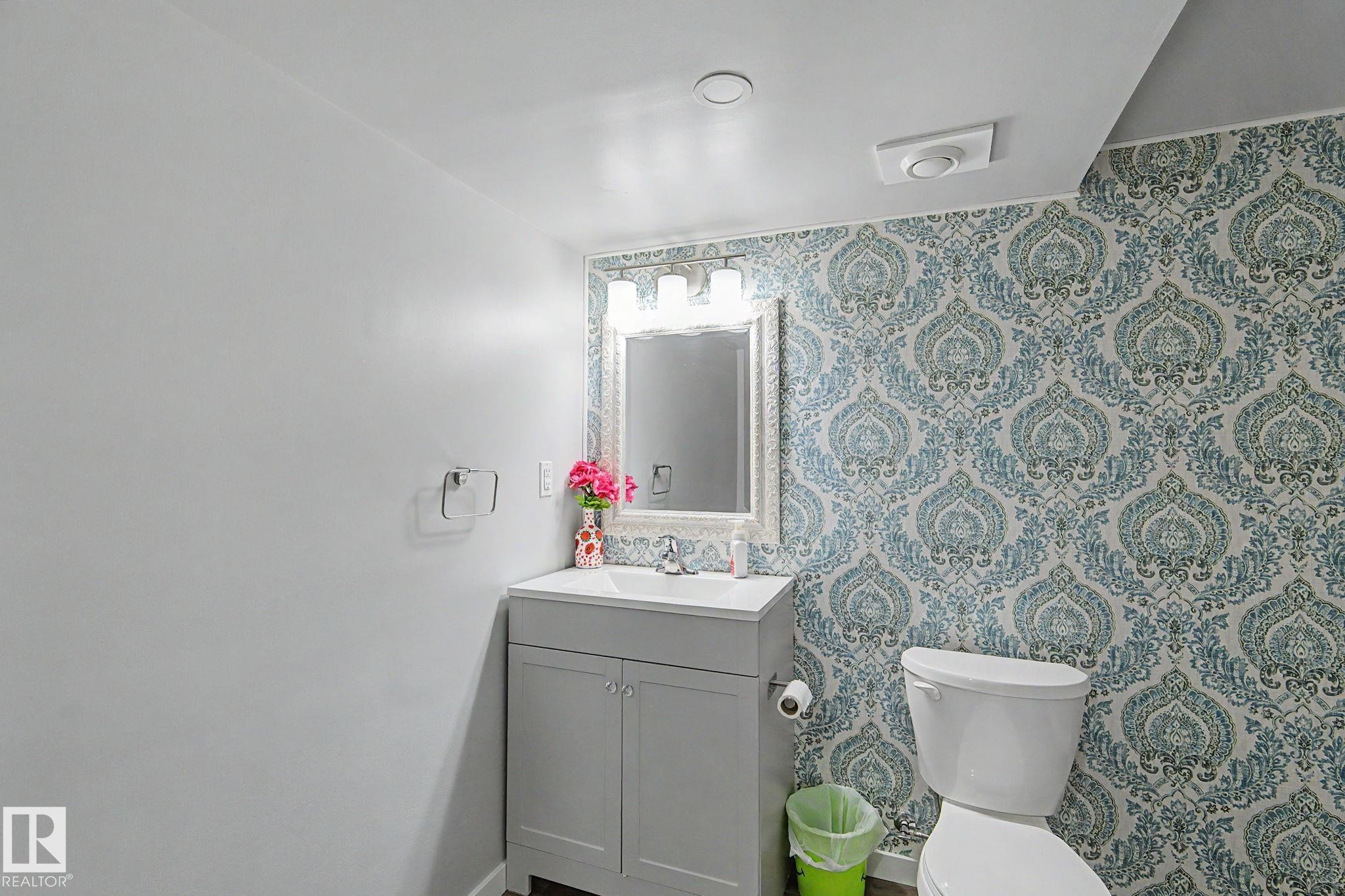 Bathroom featuring a patterned accent wall, white toilet, and a vanity with a rectangular sink - 18144 76 Street Nw, Edmonton, AB - Indoor Photo Showing Bathroom