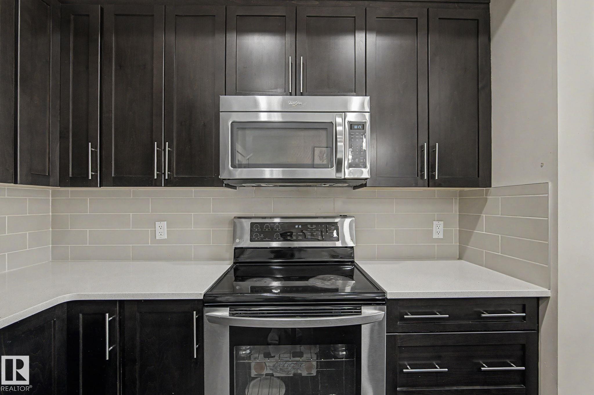 Kitchen featuring dark wood-finish cabinetry, light-toned countertops, and a subway tile backsplash - 18144 76 Street Nw, Edmonton, AB - Indoor Photo Showing Kitchen