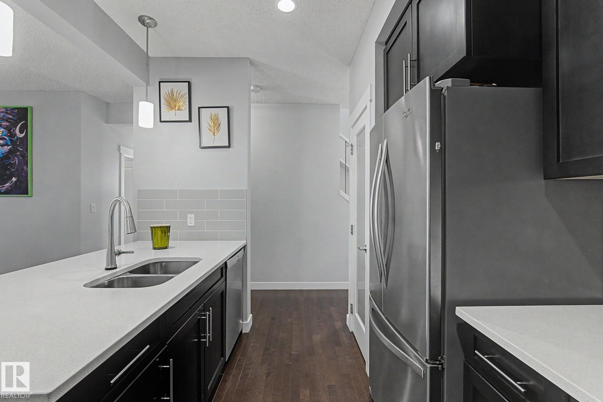 Modern kitchen featuring dark wood cabinetry, stainless steel appliances, white countertops, and wood-finish flooring - 18144 76 Street Nw, Edmonton, AB - Indoor Photo Showing Kitchen With Double Sink