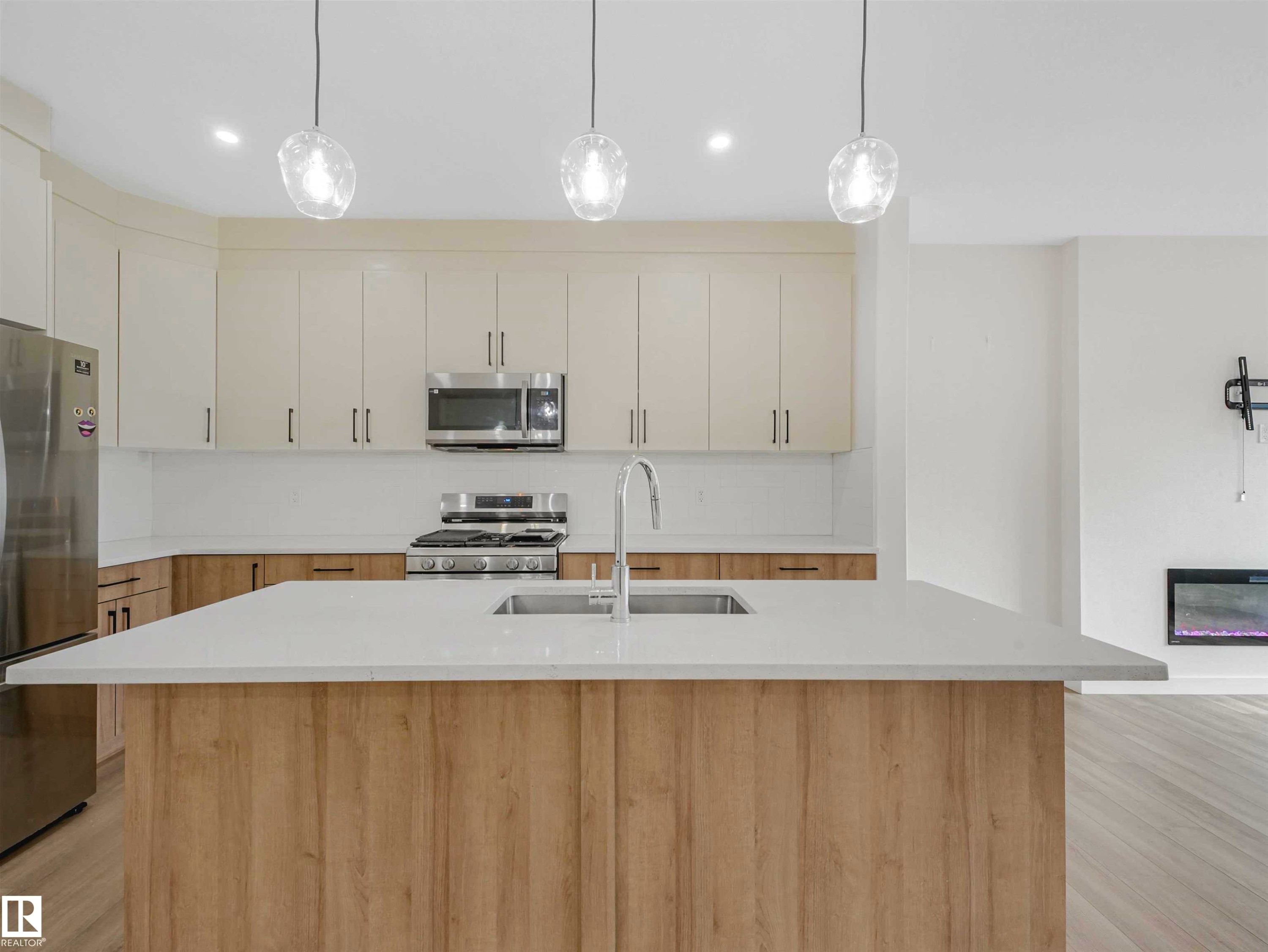 Contemporary kitchen featuring a large island with an undermount sink, pendant lighting, stainless steel appliances, and a built-in fireplace - 1518 Siskin Link Link, Edmonton, AB - Indoor Photo Showing Kitchen With Double Sink With Upgraded Kitchen