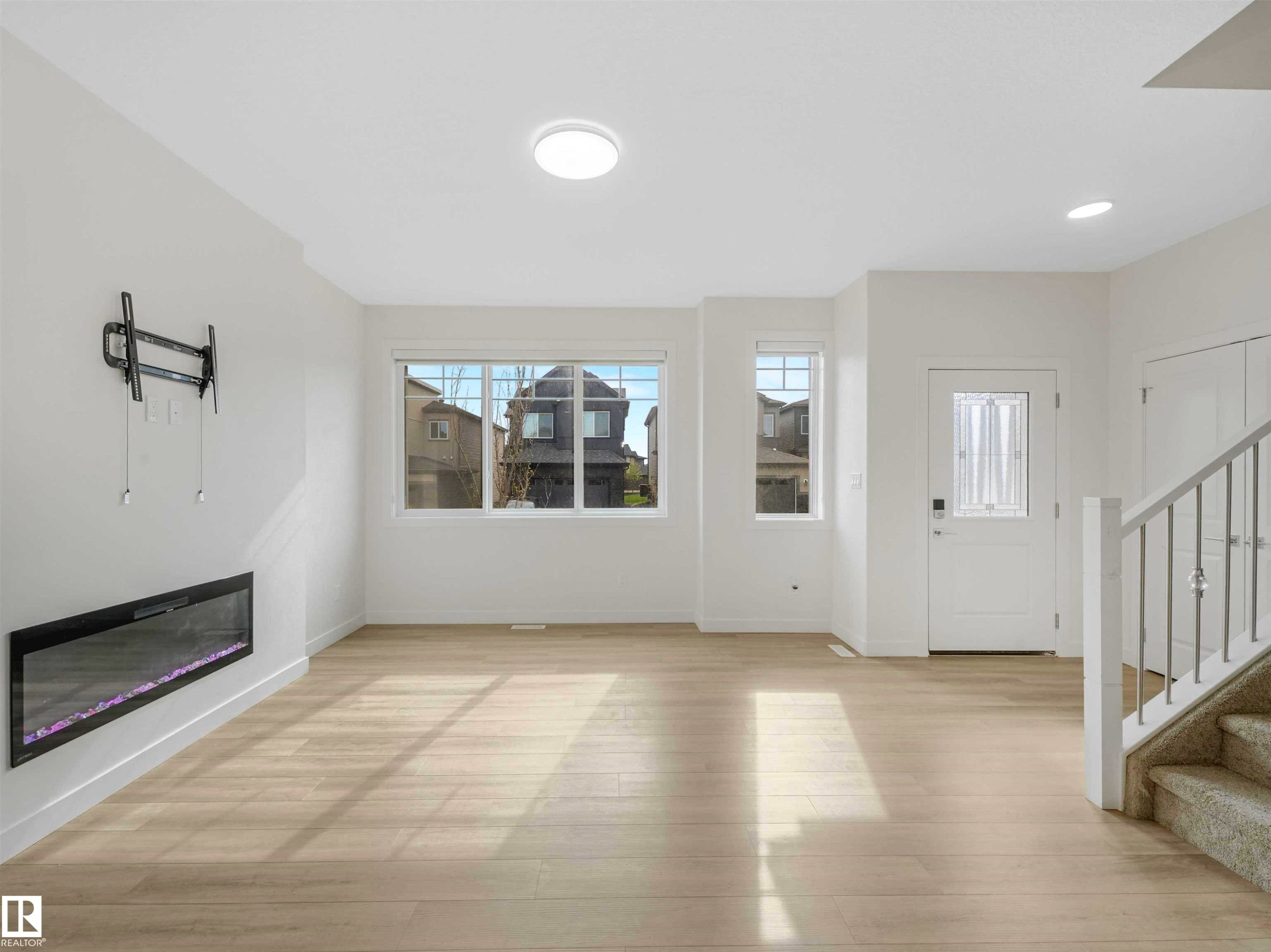 Bright living area featuring wood-finish flooring, an electric fireplace, white trim, and a staircase with a metal railing - 1518 Siskin Link Link, Edmonton, AB - Indoor With Fireplace