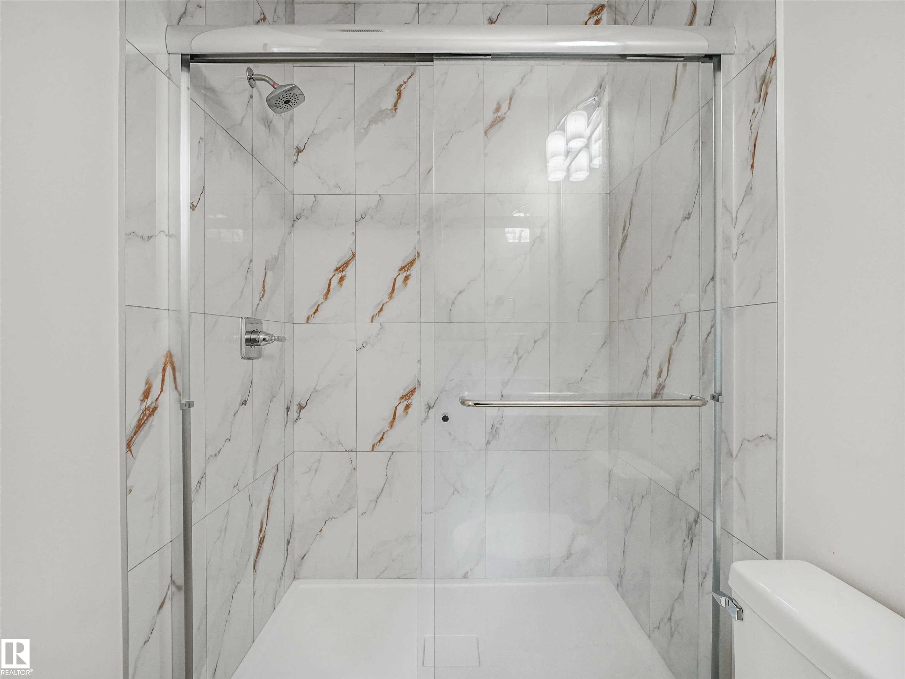 Glass-enclosed shower featuring white and gold veined tile, a white shower pan, a rainfall showerhead, and a chrome grab bar - 1518 Siskin Link Link, Edmonton, AB - Indoor Photo Showing Bathroom