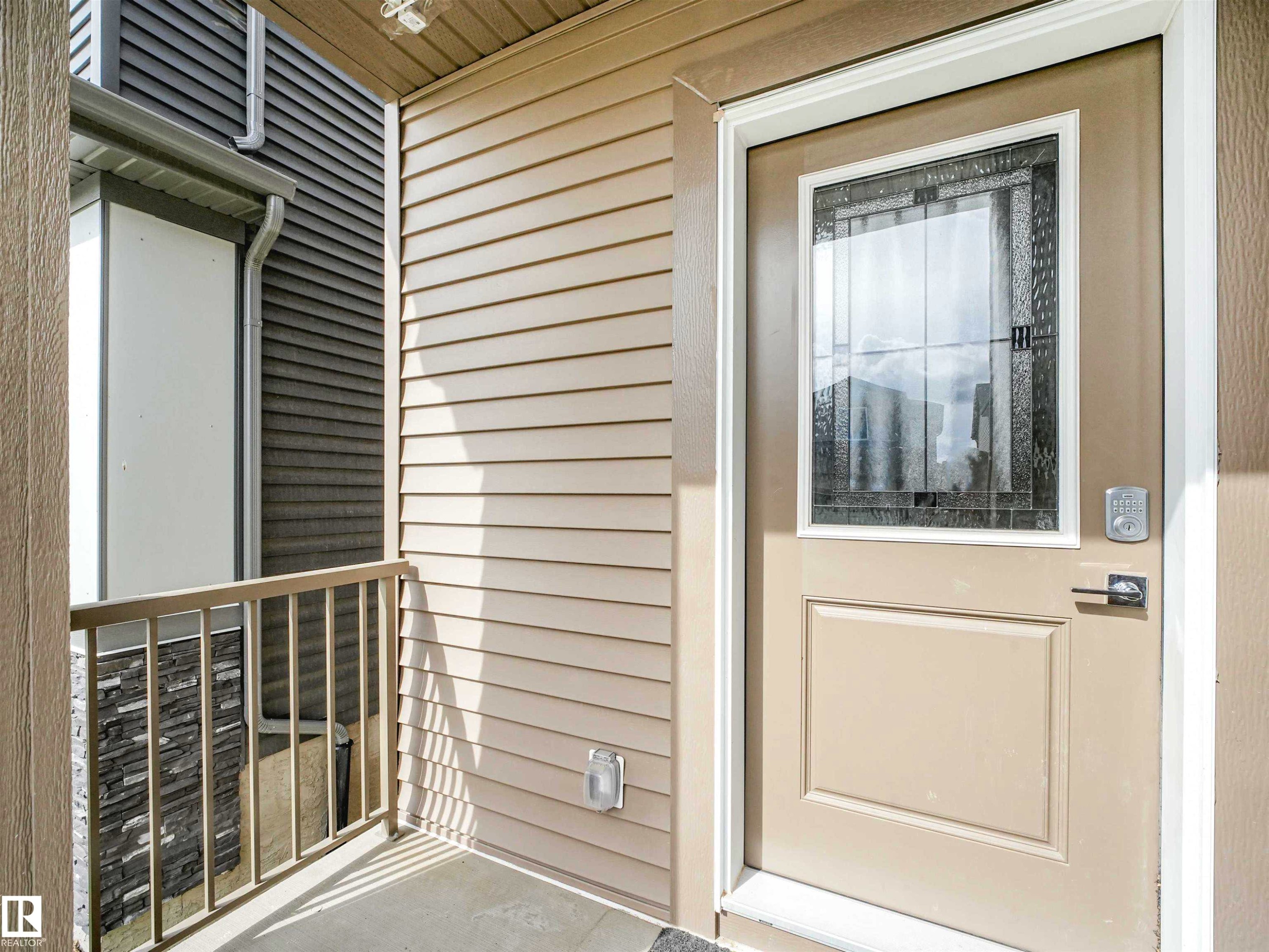 Entryway featuring a decorative glass door, light-colored siding, and a metal railing - 1518 Siskin Link Link, Edmonton, AB - Outdoor With Exterior