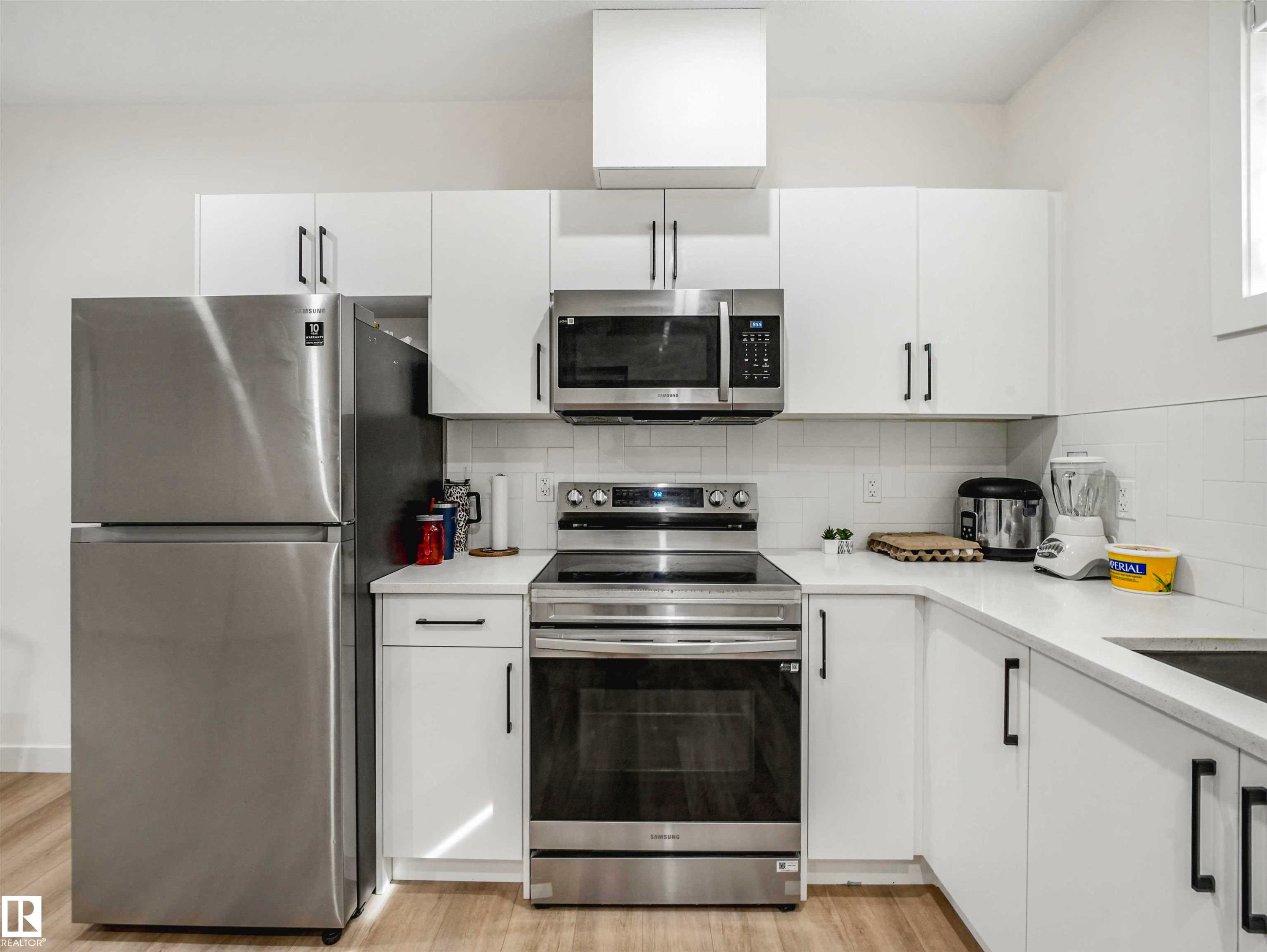 Modern kitchen featuring white cabinetry, stainless steel appliances, a white subway tile backsplash, light-toned countertops, and wood-finish flooring - 1518 Siskin Link Link, Edmonton, AB - Indoor Photo Showing Kitchen