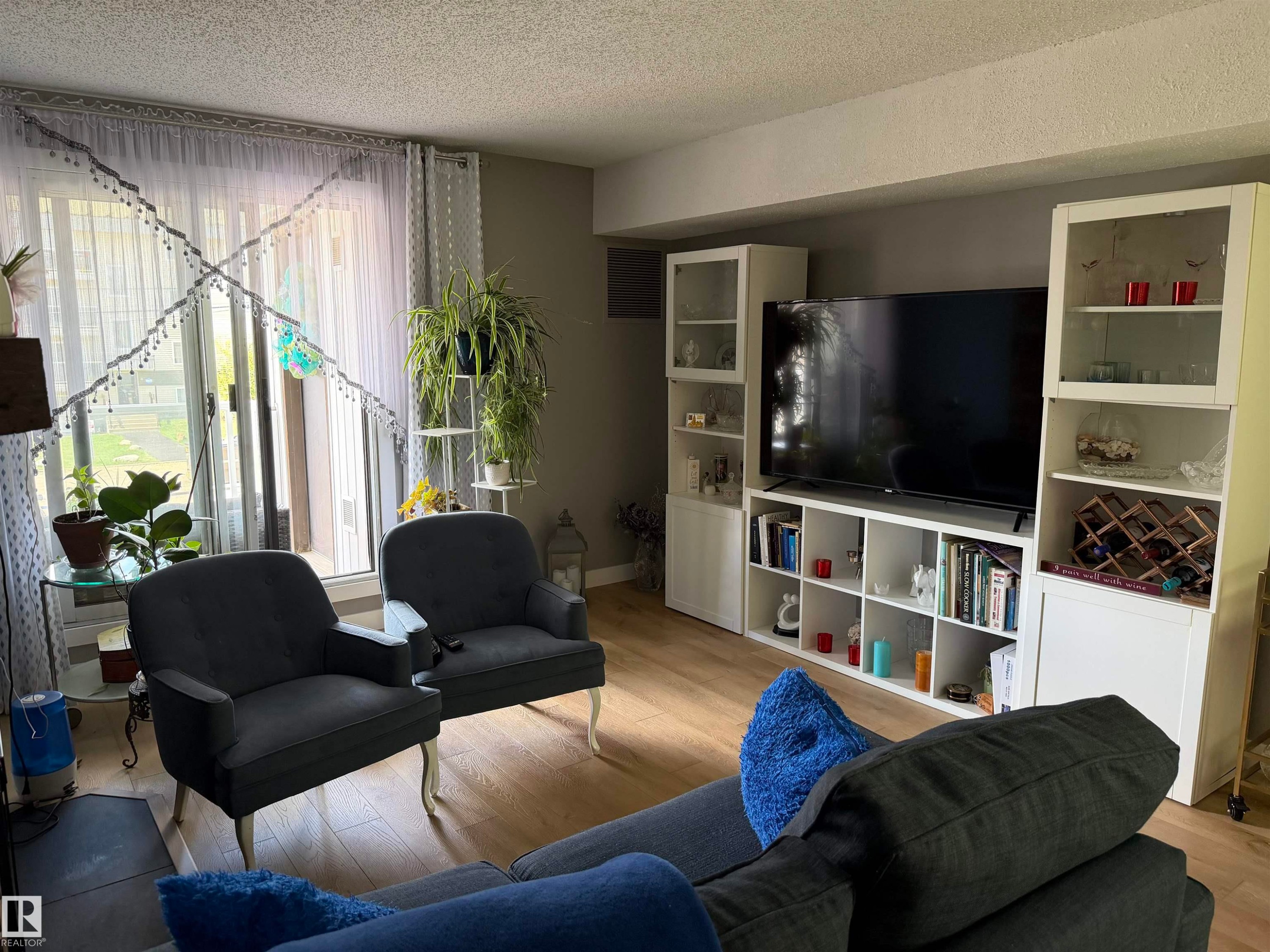 Living area featuring wood-finish flooring, a full-wall built-in media center, and expansive glass doors opening to the outdoors - 205 10604 110 Avenue Nw, Edmonton, AB - Indoor Photo Showing Living Room