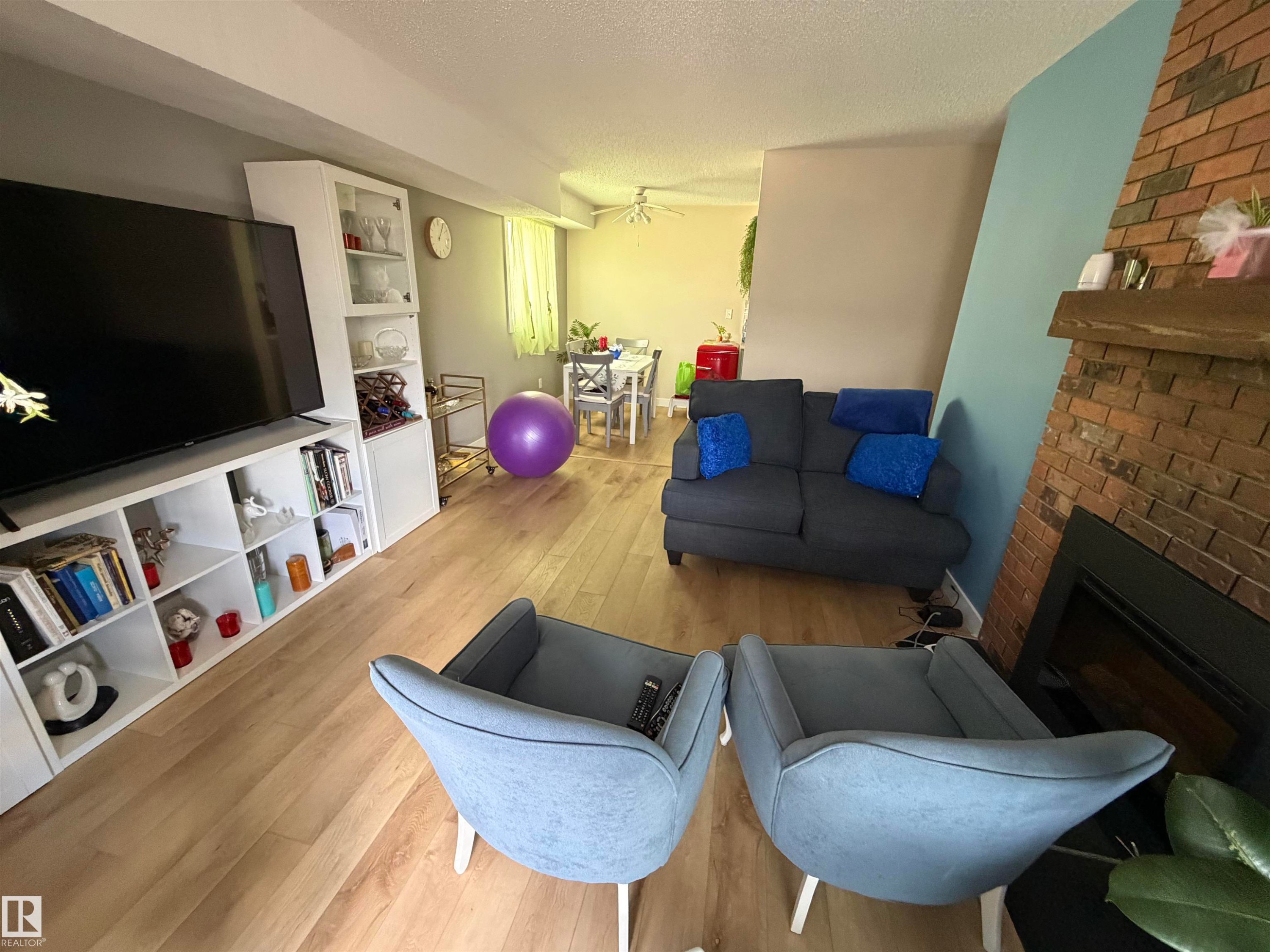 Living area featuring wood-finish flooring, a brick-surround fireplace with a wood mantle, and a built-in entertainment center with open shelving and cabinet storage - 205 10604 110 Avenue Nw, Edmonton, AB - Indoor Photo Showing Living Room With Fireplace