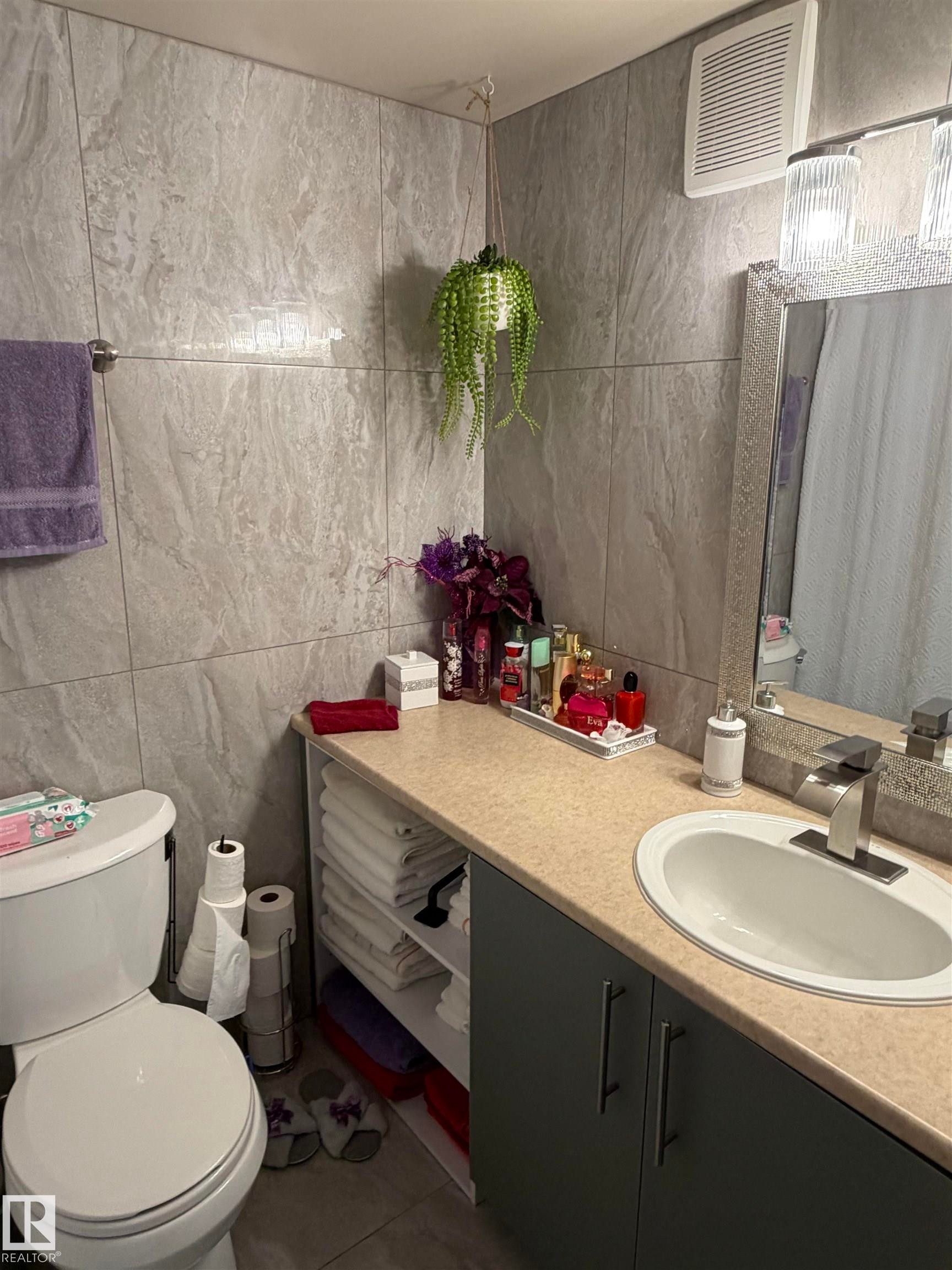 Bathroom featuring a vanity with integrated sink and chrome faucet, under-sink cabinetry, open shelving, and a toilet - 205 10604 110 Avenue Nw, Edmonton, AB - Indoor Photo Showing Bathroom