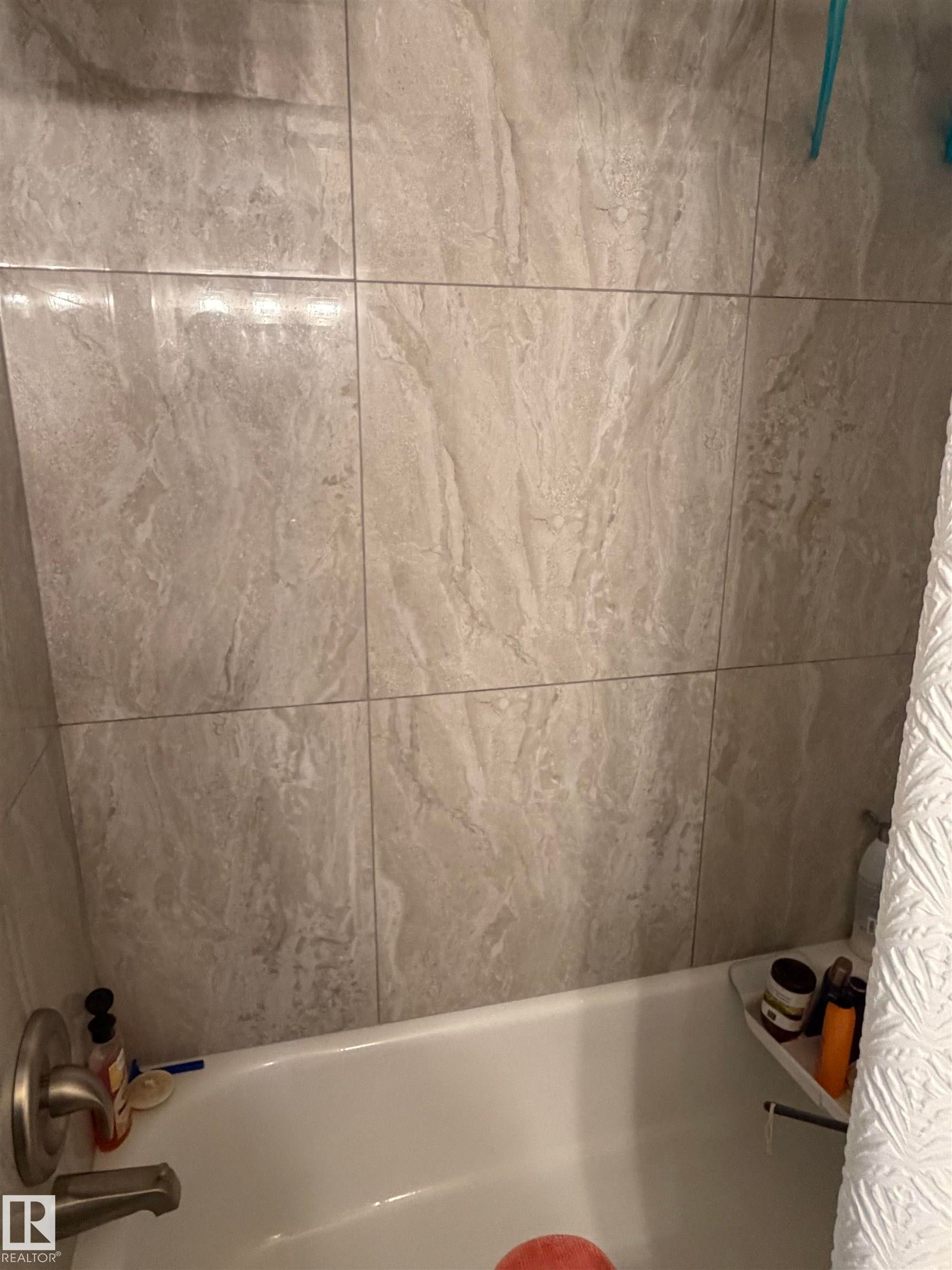 Bathtub with brushed nickel fixtures and light-toned tile surround - 205 10604 110 Avenue Nw, Edmonton, AB - Indoor Photo Showing Bathroom