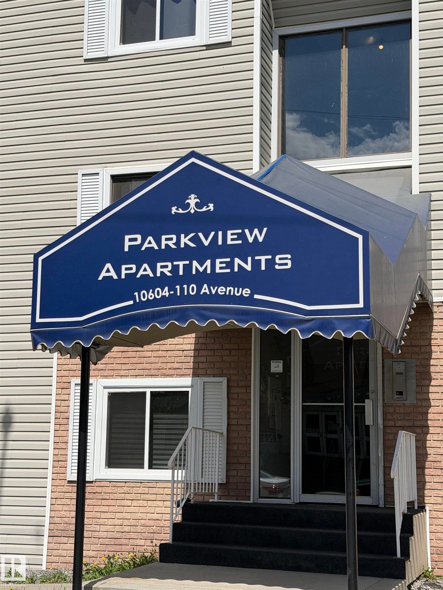 Building entrance featuring a navy awning, brick facade, and light-colored siding - 205 10604 110 Avenue Nw, Edmonton, AB - Outdoor With Exterior