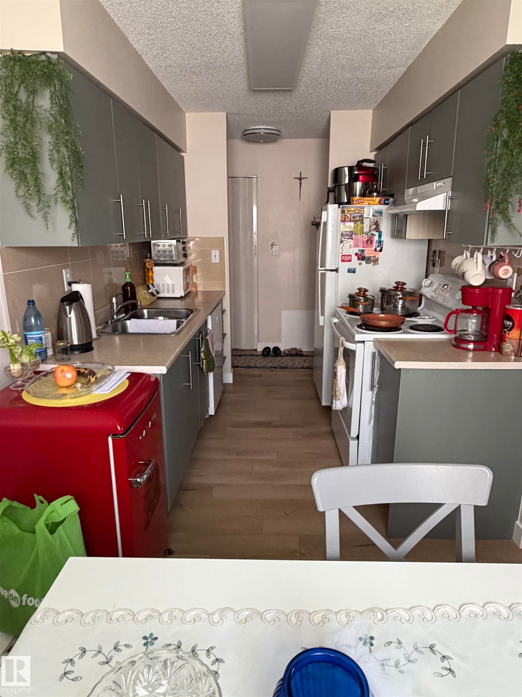Galley kitchen featuring wood-finish flooring, two walls of cabinetry, an integrated sink, and an electric range - 205 10604 110 Avenue Nw, Edmonton, AB - Indoor Photo Showing Kitchen With Double Sink