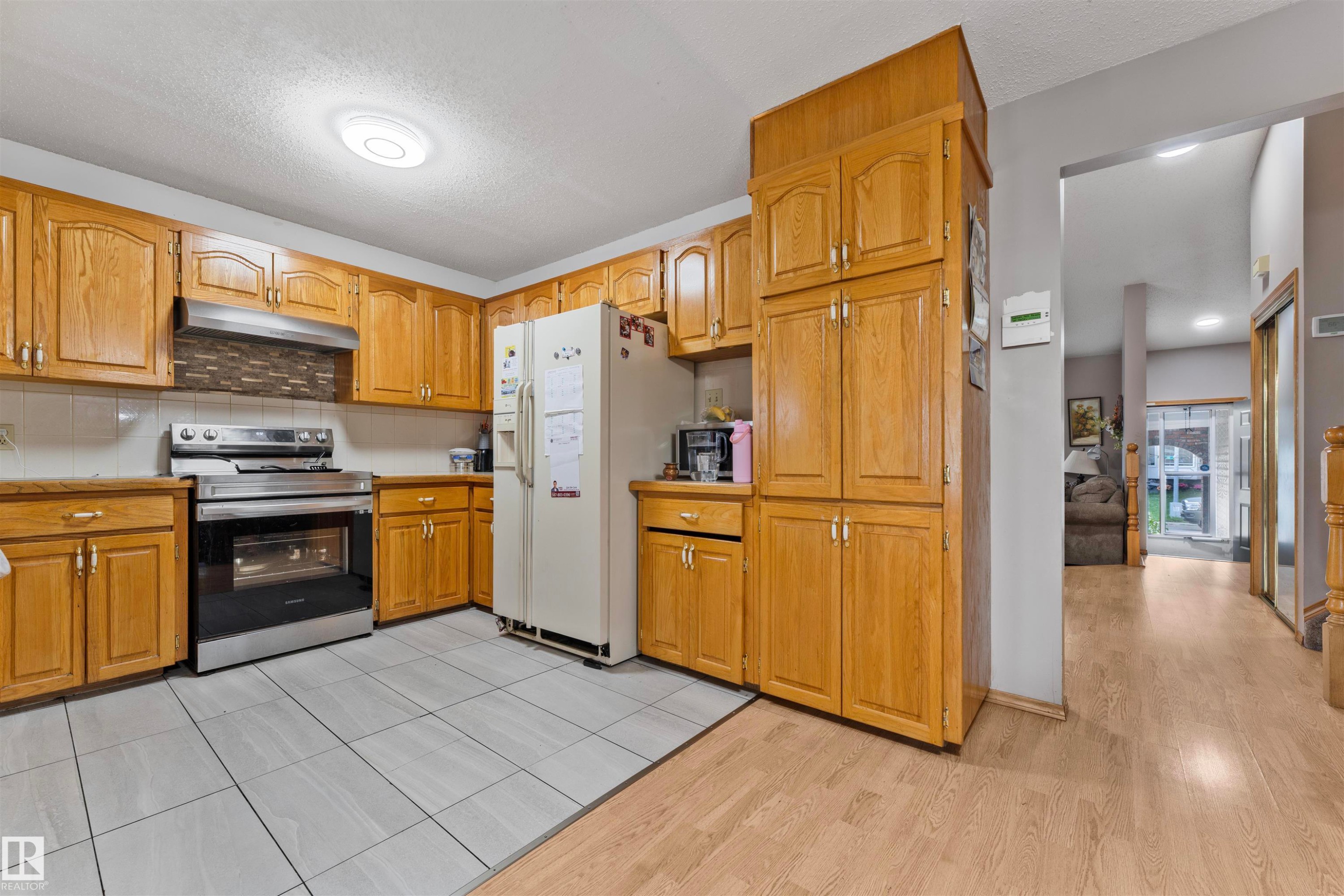 Kitchen featuring extensive wood cabinetry, tile flooring, stainless steel range with overhead hood, and a decorative tile backsplash - 4231 32 Avenue, Edmonton, AB - Indoor Photo Showing Kitchen
