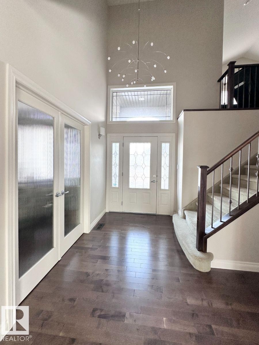 Spacious entryway featuring dark wood-finish flooring, a two-story ceiling, a contemporary chandelier, a front door with decorative glass, and a staircase with dark wood railing and balusters - 820 Drysdale Run, Edmonton, AB - Indoor Photo Showing Other Room
