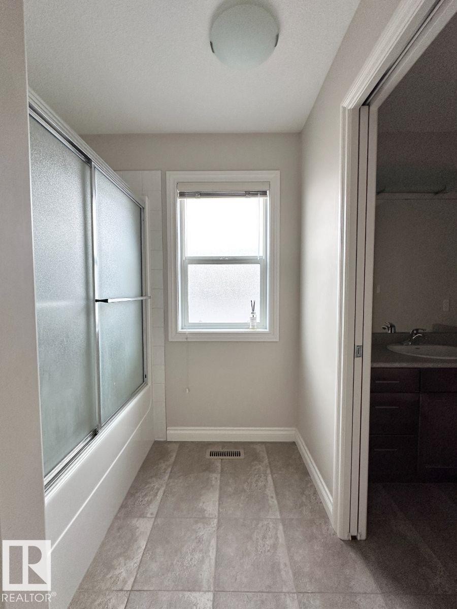 Bathroom featuring a tub/shower combination with sliding frosted glass doors, a single window, recessed lighting, and tile flooring - 820 Drysdale Run, Edmonton, AB - Indoor Photo Showing Other Room