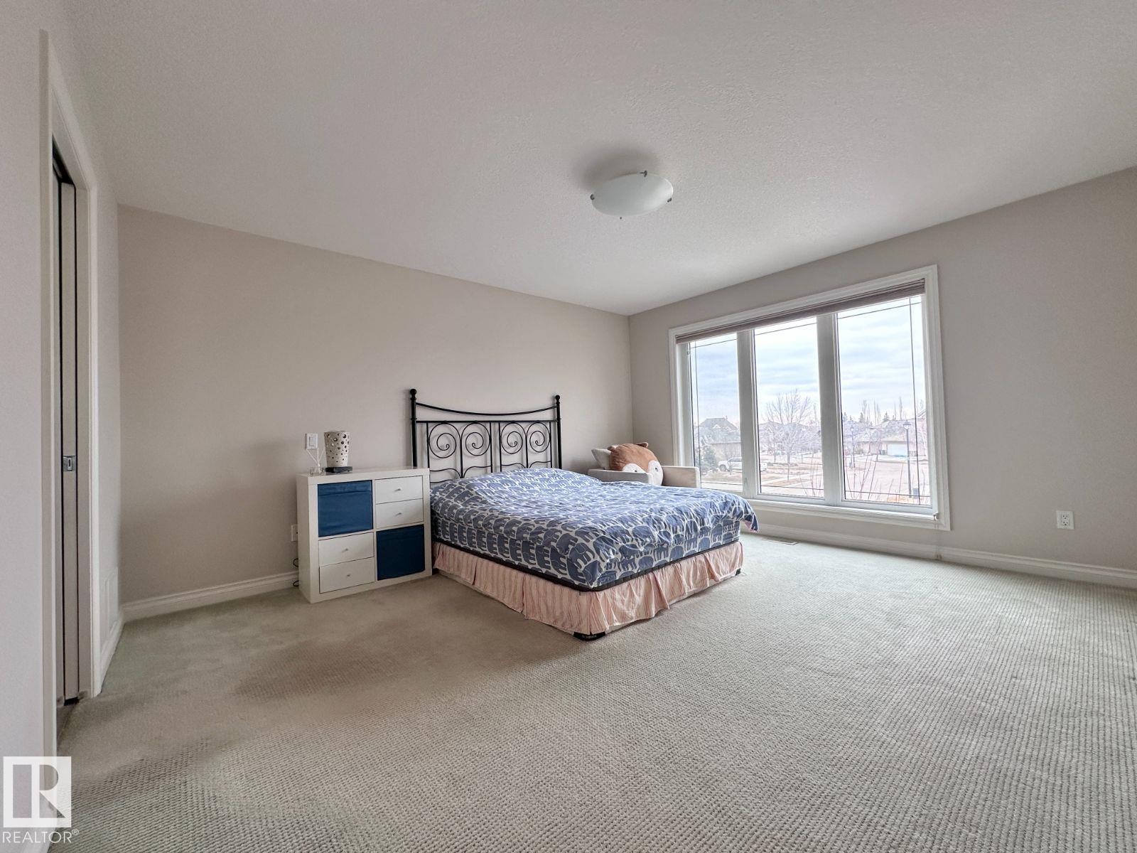 Spacious room featuring neutral wall tones, plush carpeting, a large multi-pane window, and a built-in closet with bifold doors - 820 Drysdale Run, Edmonton, AB - Indoor Photo Showing Bedroom