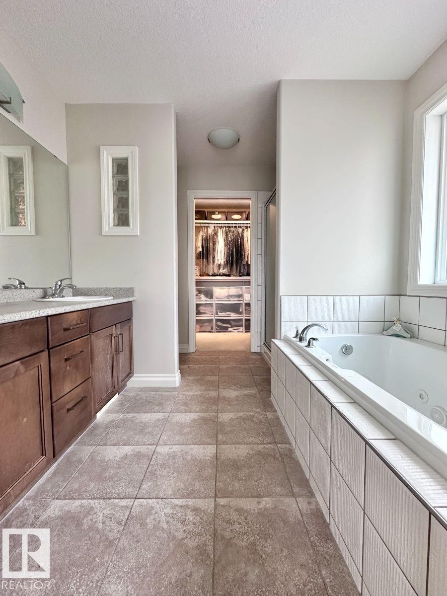 Spacious bathroom featuring a dual vanity with wood-finish cabinetry, a large jetted tub with tile surround, and a walk-in closet with built-in organization - 820 Drysdale Run, Edmonton, AB - Indoor Photo Showing Bathroom