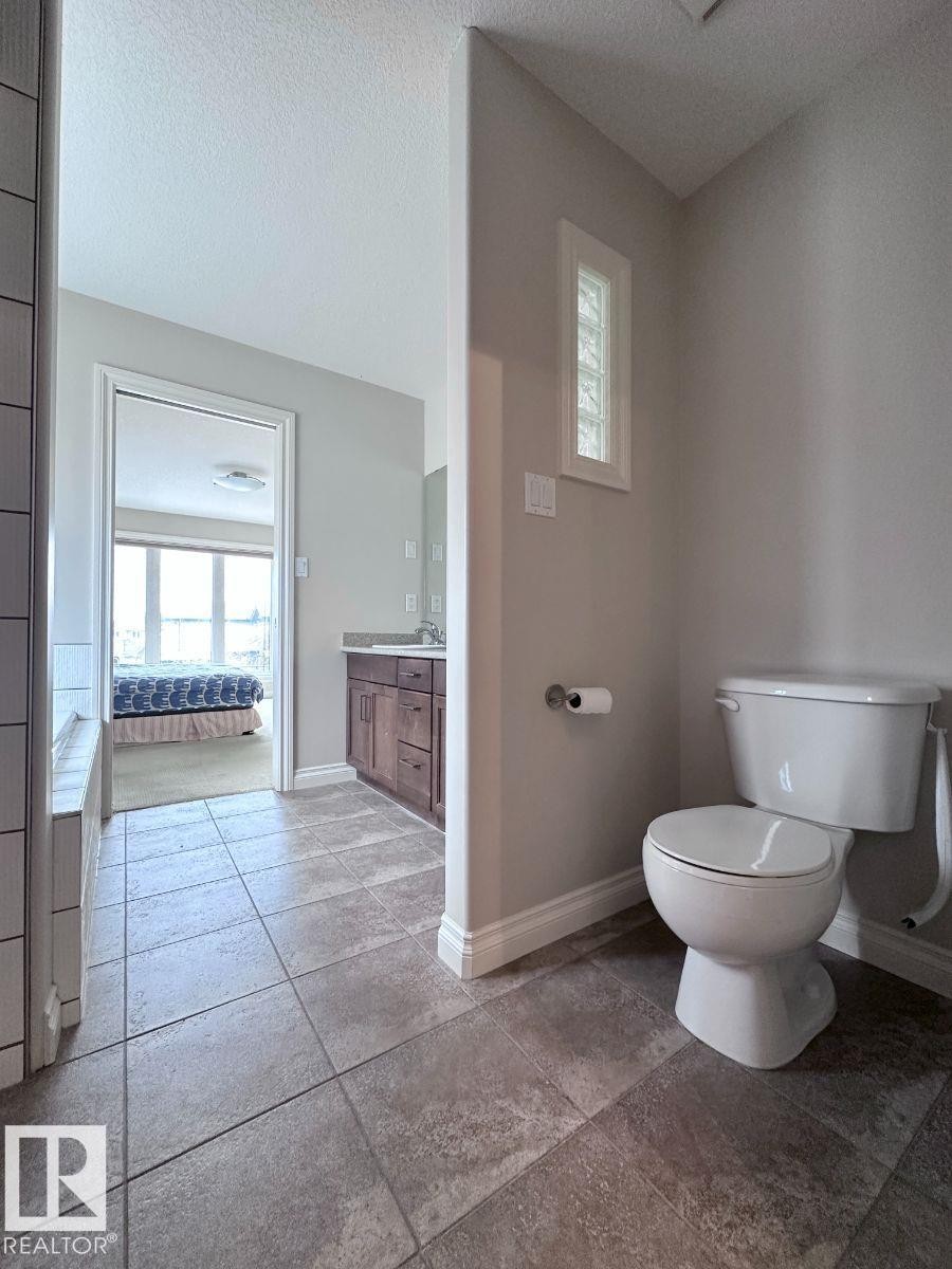 Bathroom featuring large format floor tiling, a white toilet, and a glass block privacy window - 820 Drysdale Run, Edmonton, AB - Indoor Photo Showing Bathroom