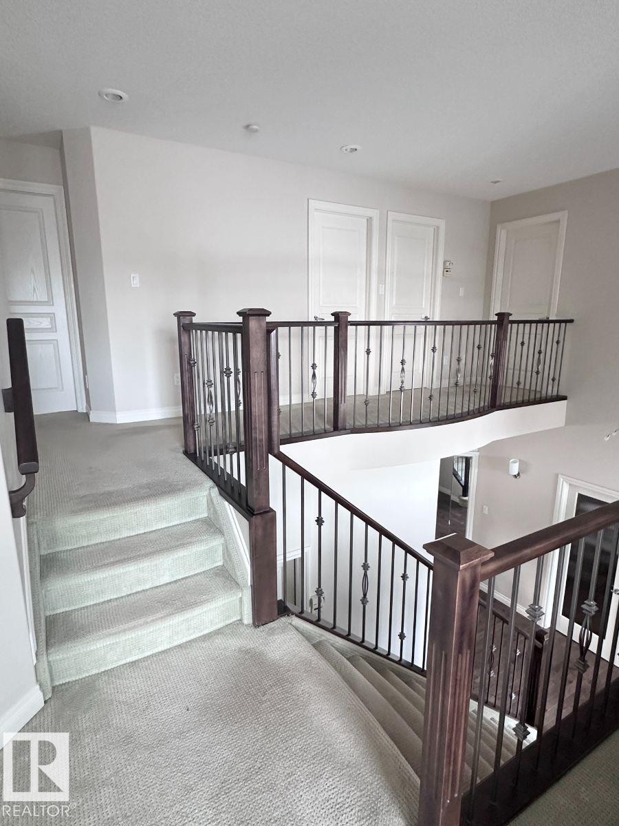 Upper-level landing featuring light-toned carpeting, dark wood-finish newel posts, and wrought iron balusters - 820 Drysdale Run, Edmonton, AB - Indoor Photo Showing Other Room