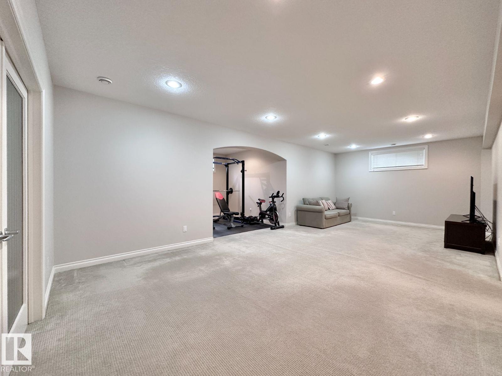 Spacious lower-level room featuring light gray carpet, recessed lighting, and an arched entryway - 820 Drysdale Run, Edmonton, AB - Indoor Photo Showing Basement