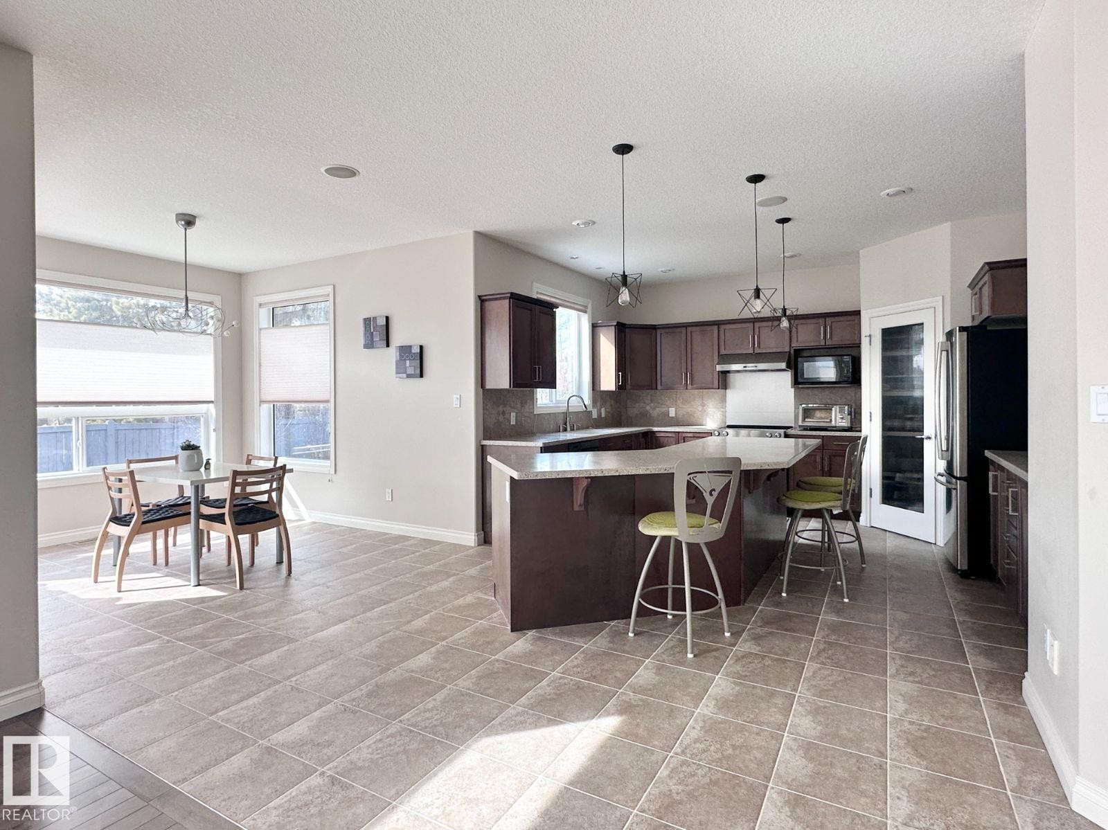 Spacious kitchen featuring an L-shaped island with seating, dark wood cabinetry, stainless steel appliances, and tile flooring - 820 Drysdale Run, Edmonton, AB - Indoor