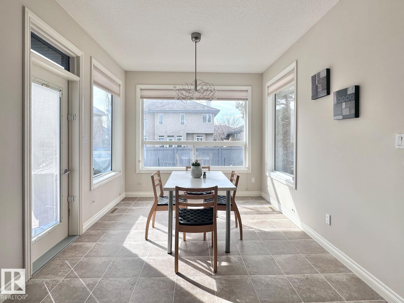 Room featuring large windows, a glass-paneled door, tile flooring, a contemporary ceiling light fixture, and light-toned wall finishes - 820 Drysdale Run, Edmonton, AB - Indoor Photo Showing Dining Room