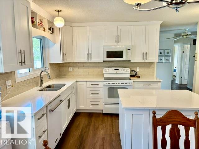 Bright kitchen featuring white shaker cabinetry, light-toned countertops, a subway tile backsplash, stainless steel sink, and wood-finish flooring - 4805 53Ave, Willingdon, AB - Indoor Photo Showing Kitchen With Double Sink