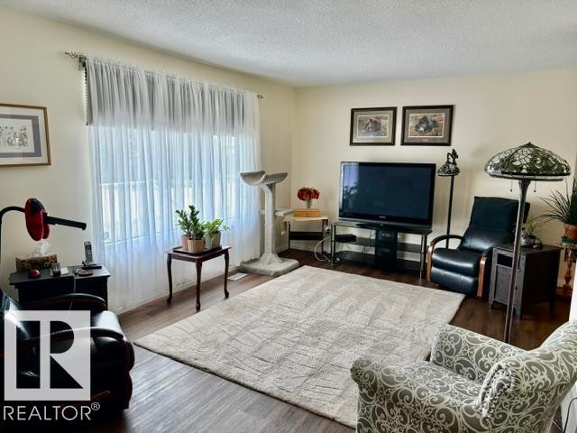 Expansive living area featuring wood-finish flooring, light-toned walls, and a large window with sheer white curtains - 4805 53Ave, Willingdon, AB - Indoor Photo Showing Living Room