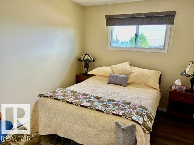 Spacious room featuring a large window with privacy shade, ample wall space, and dark wood-finish flooring - 4805 53Ave, Willingdon, AB - Indoor Photo Showing Bedroom