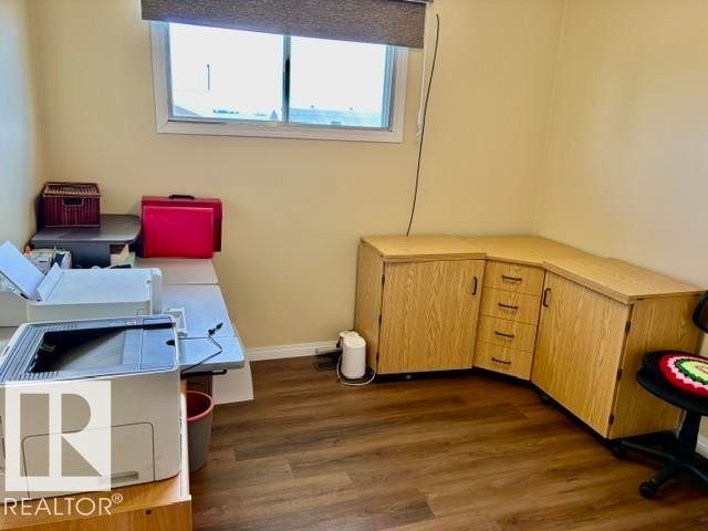 Dedicated workspace featuring wood-finish flooring, built-in cabinetry, corner desk configuration, and an overhead window with roller shade - 4805 53Ave, Willingdon, AB - Indoor Photo Showing Office