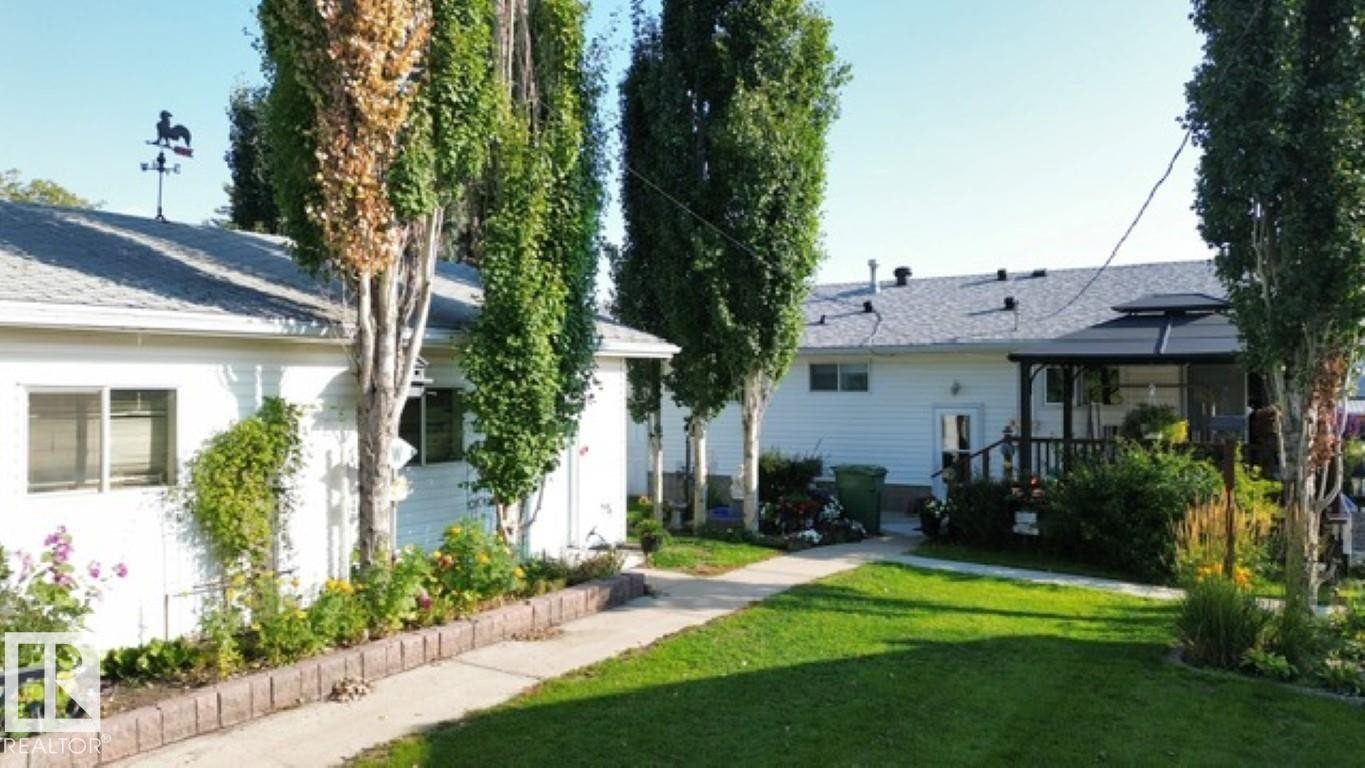 Expansive green lawn with a concrete pathway leading to two white-sided structures - 4805 53Ave, Willingdon, AB - Outdoor