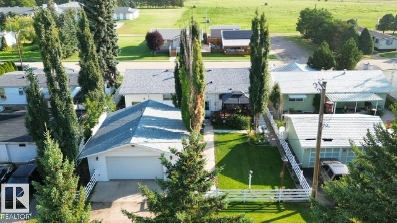 Property featuring a front-facing garage with a white door, a well-maintained lawn, a white picket fence, and mature trees - 4805 53Ave, Willingdon, AB - Outdoor