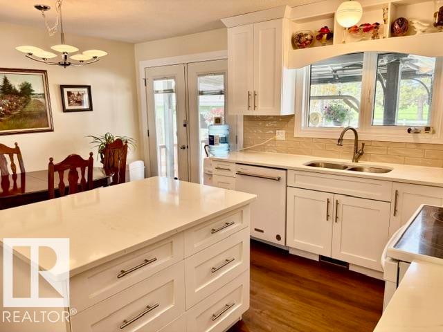 Kitchen featuring a central island with a light-toned countertop, white cabinetry with silver-tone hardware, wood-finish flooring, and a double-basin sink with a gooseneck faucet - 4805 53Ave, Willingdon, AB - Indoor
