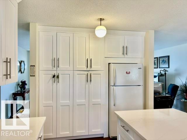 Kitchen featuring extensive white shaker cabinetry, stainless steel hardware, a built-in refrigerator recess, white countertops, and a ceiling-mounted globe light fixture - 4805 53Ave, Willingdon, AB - Indoor Photo Showing Kitchen