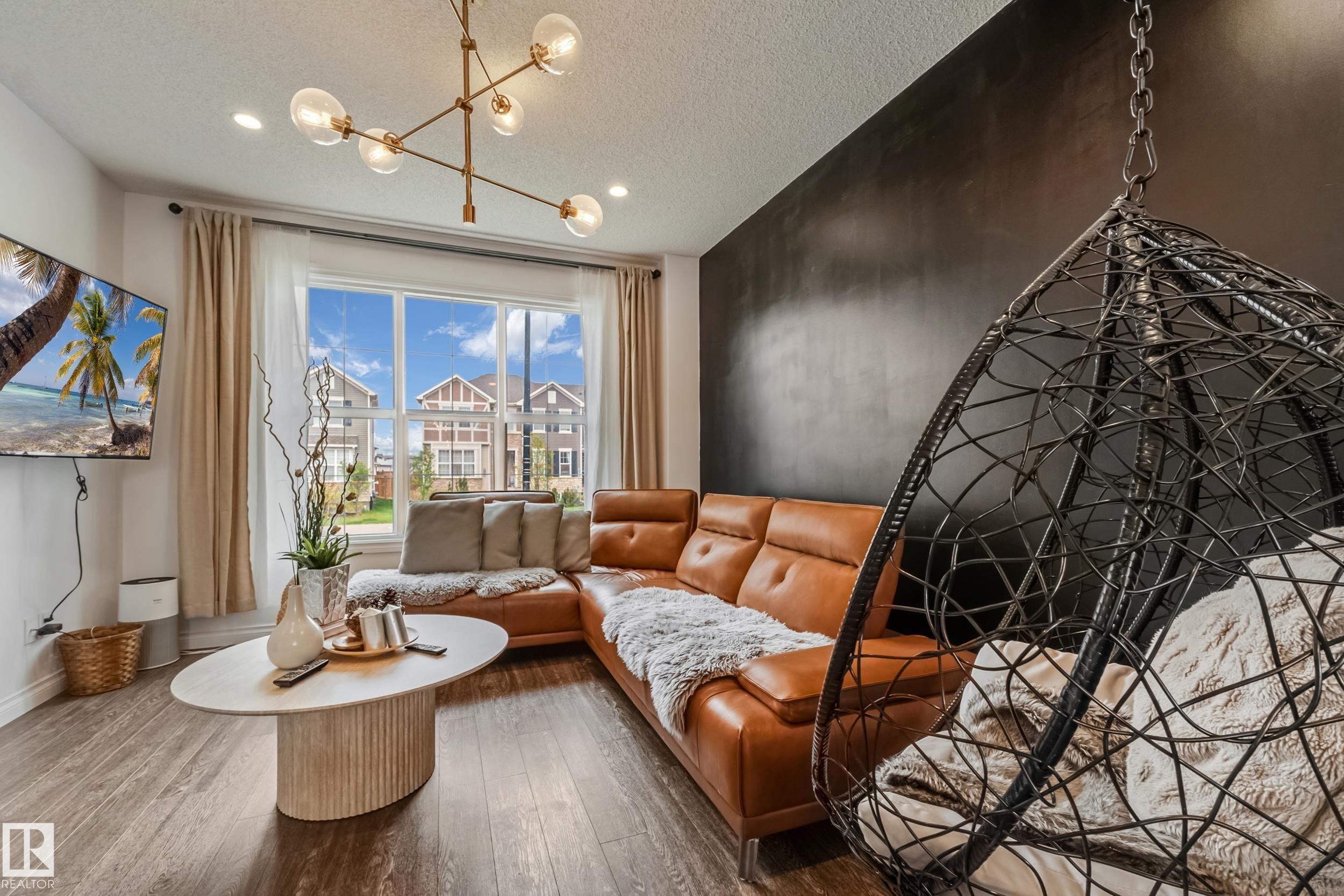 Living area featuring wood-finish flooring, a large window with white trim, and a modern linear chandelier - 8131 Chappelle Way, Edmonton, AB - Indoor Photo Showing Other Room