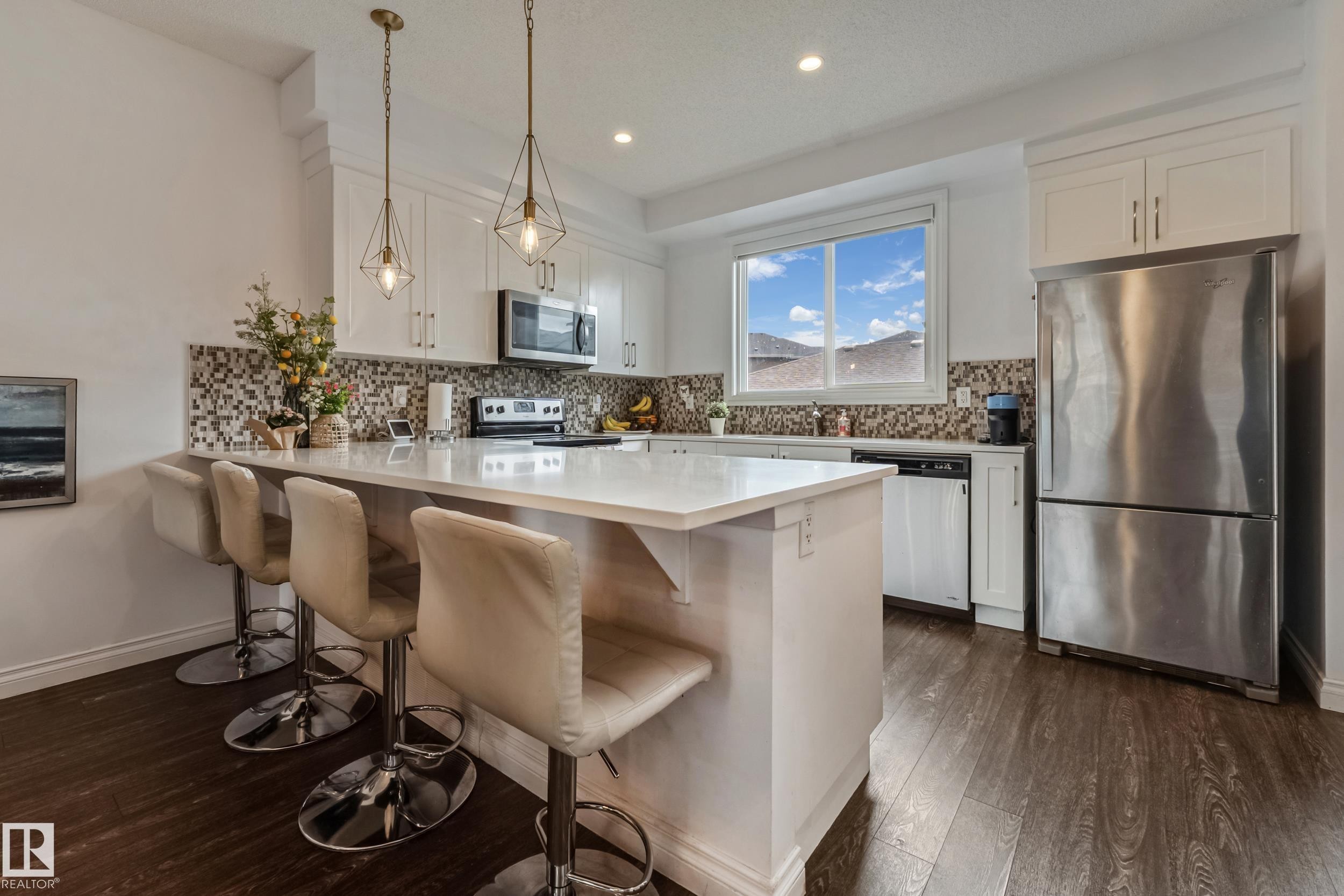 Kitchen featuring an island with white countertop, white cabinetry, a mosaic tile backsplash, stainless steel appliances, and dark wood-finish flooring - 8131 Chappelle Way, Edmonton, AB - Indoor Photo Showing Kitchen With Upgraded Kitchen