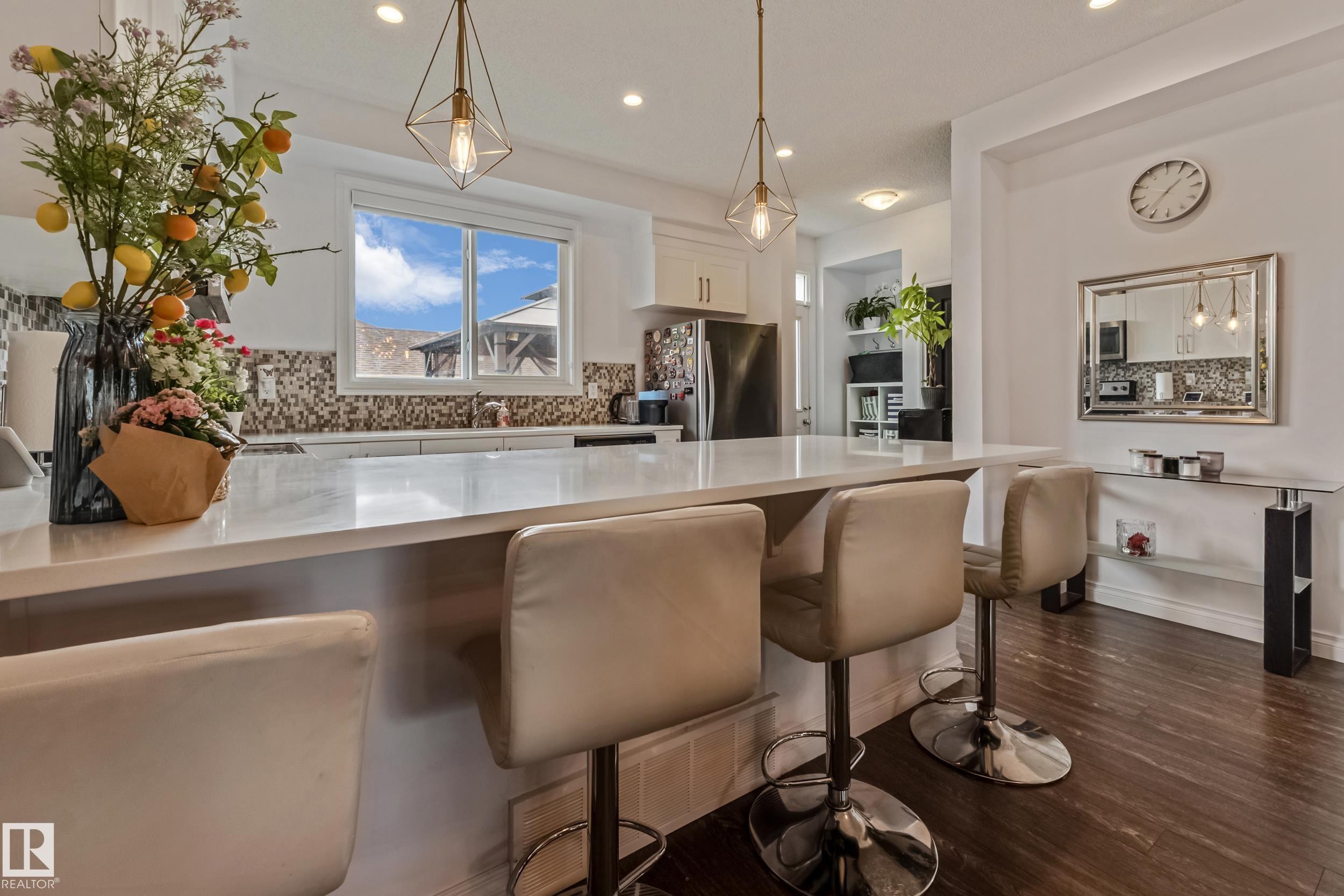Kitchen island featuring a substantial countertop, pendant lighting, white cabinetry, and stainless steel appliances - 8131 Chappelle Way, Edmonton, AB - Indoor